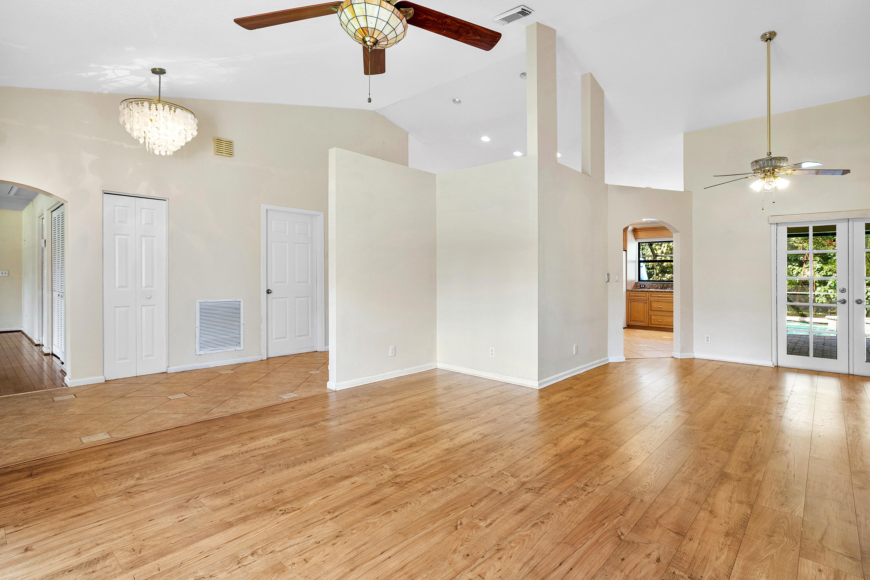 Open-concept room featuring vaulted ceilings, wood-finish flooring, dual ceiling fans, a crystal-style chandelier, and glass-paneled double doors