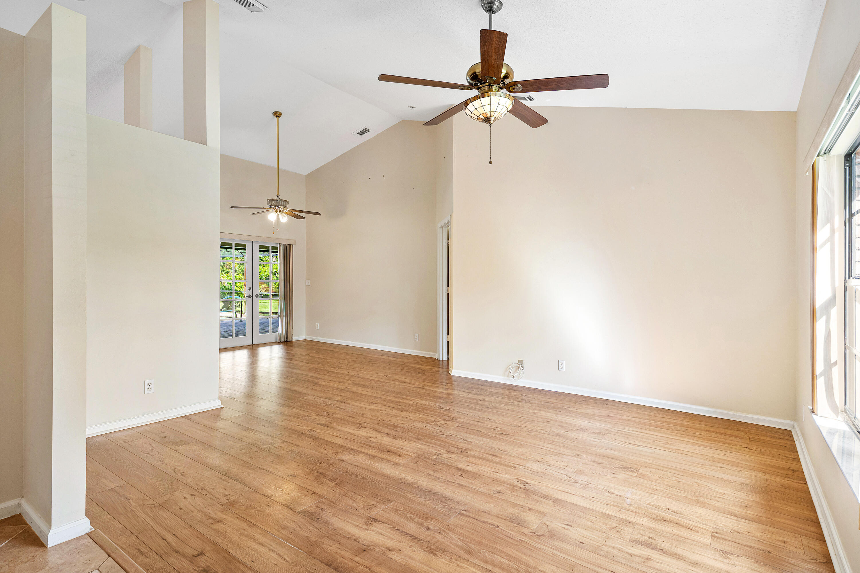 Vaulted ceilings, wood-finish flooring, dual ceiling fans with integrated lighting, and multi-panel French doors