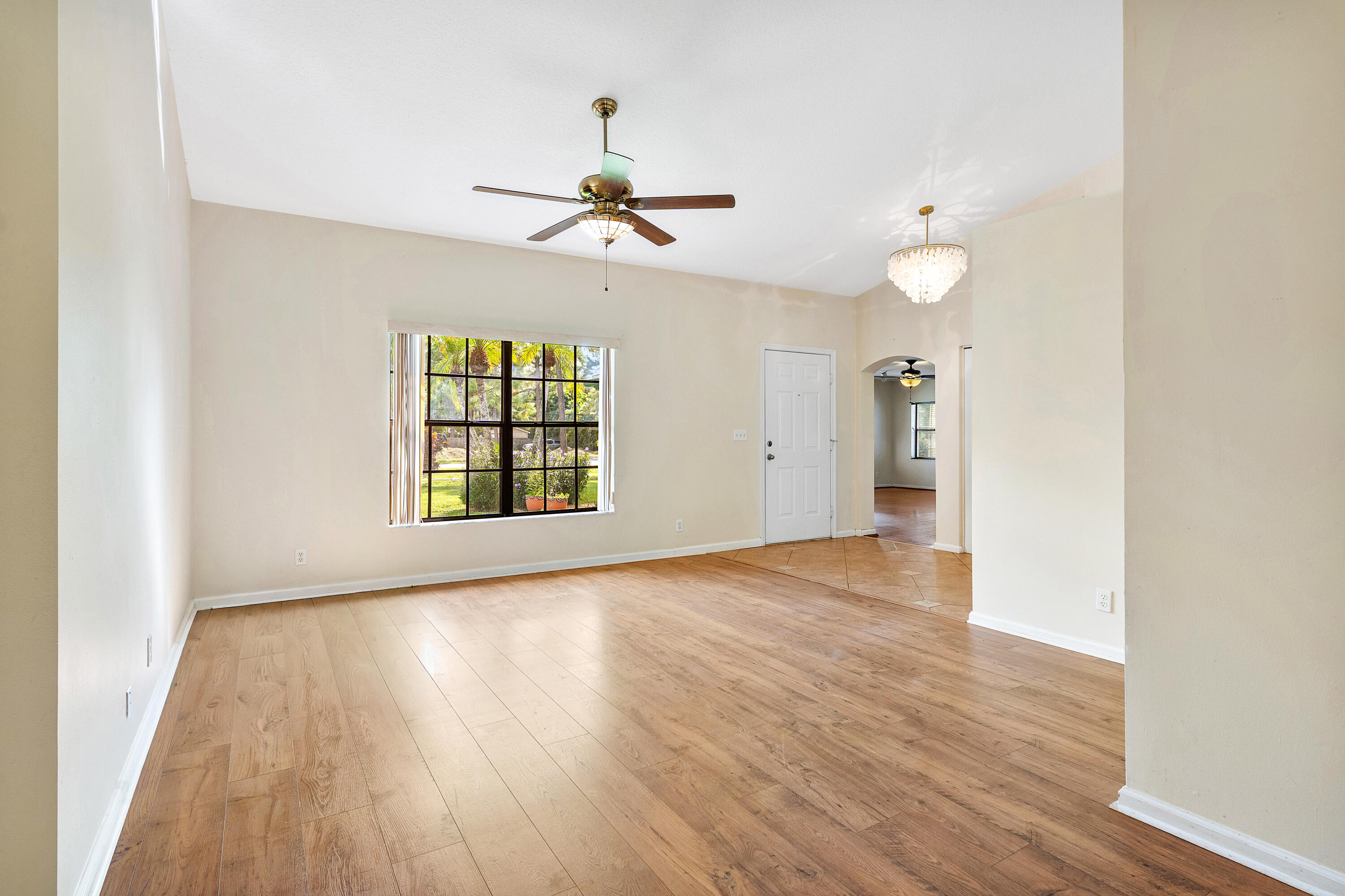 Living area featuring wood-finish flooring, high ceilings, a central ceiling fan with integrated lighting, a multi-pane window, and a decorative chandelier