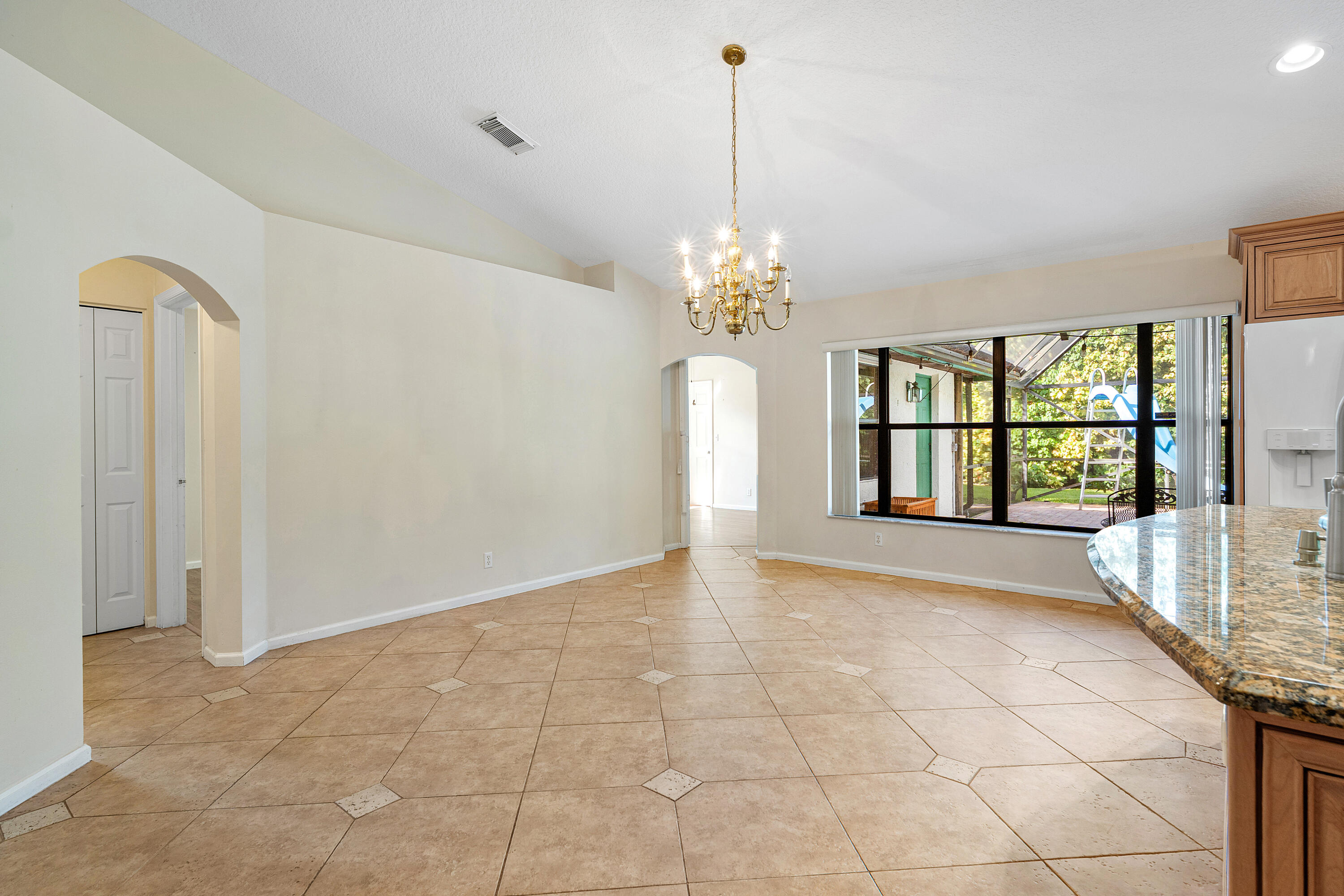 Open interior featuring vaulted ceilings, tile flooring with decorative inserts, a central multi-arm chandelier, arched entryways, and a large multi-pane window
