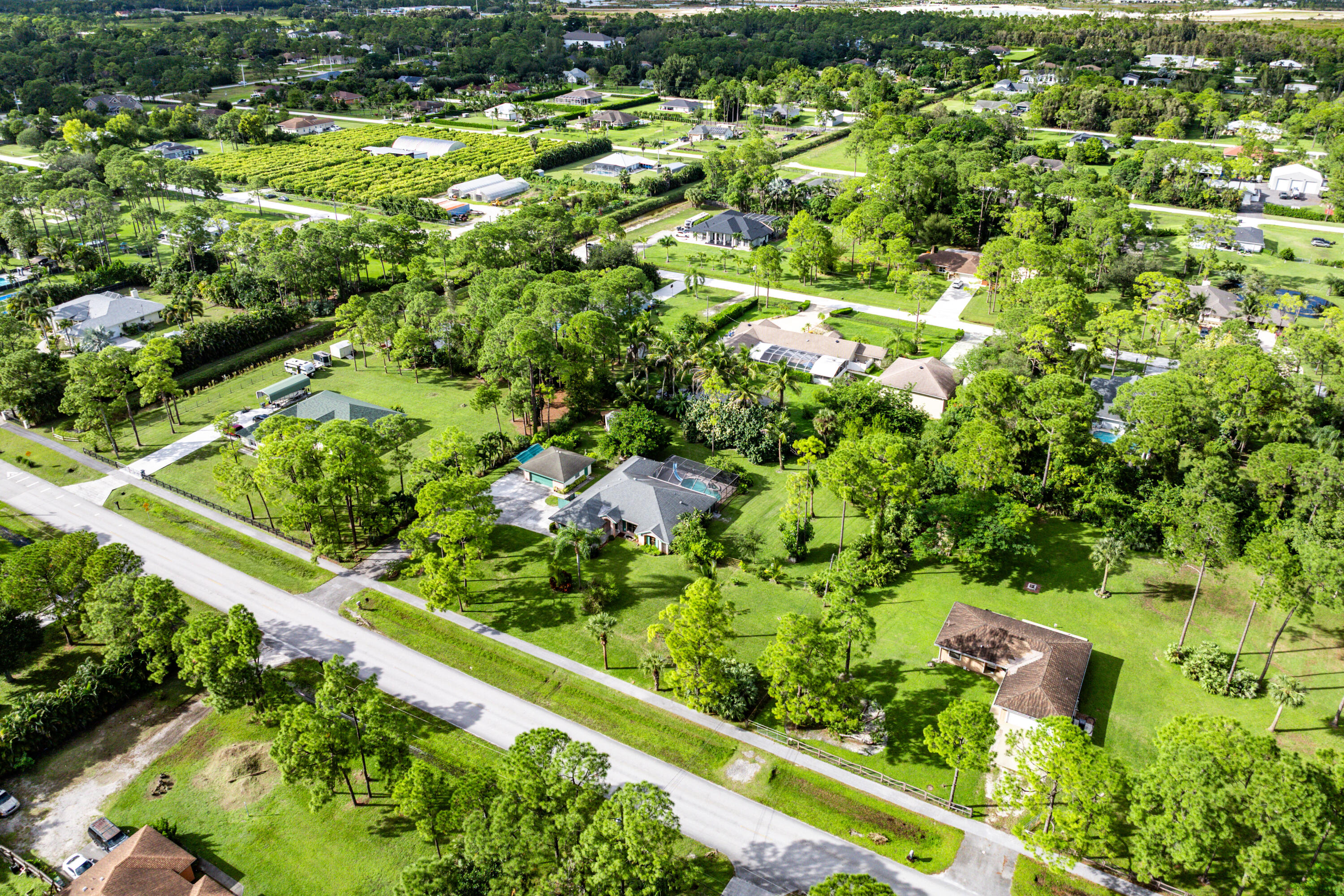 Aerial perspective of a sprawling property featuring mature trees, manicured lawns, a swimming pool, and a multi-car driveway
