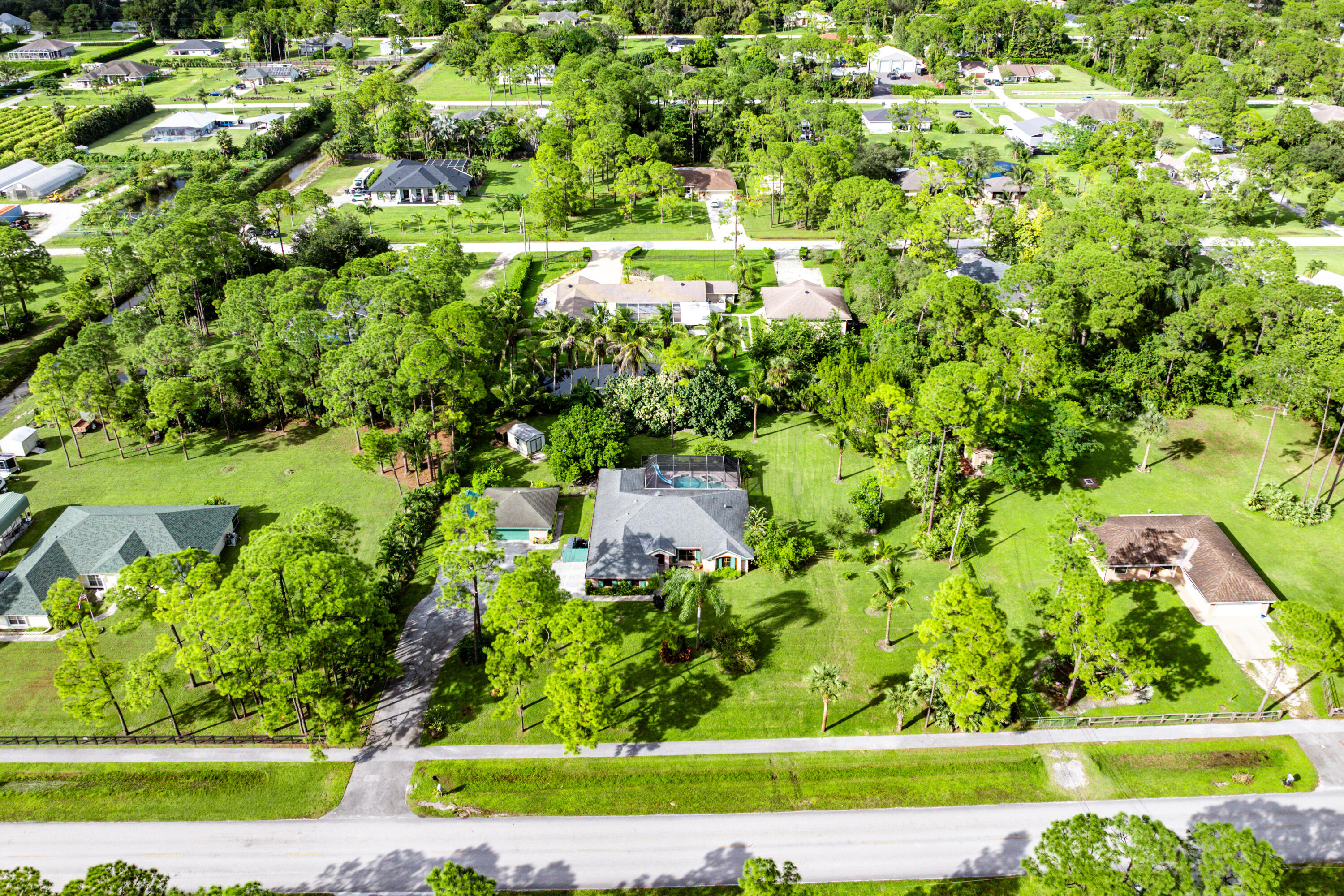 Aerial perspective of a sprawling property featuring a multi-gabled residence, an enclosed pool area, a detached auxiliary structure, and expansive grounds with mature trees