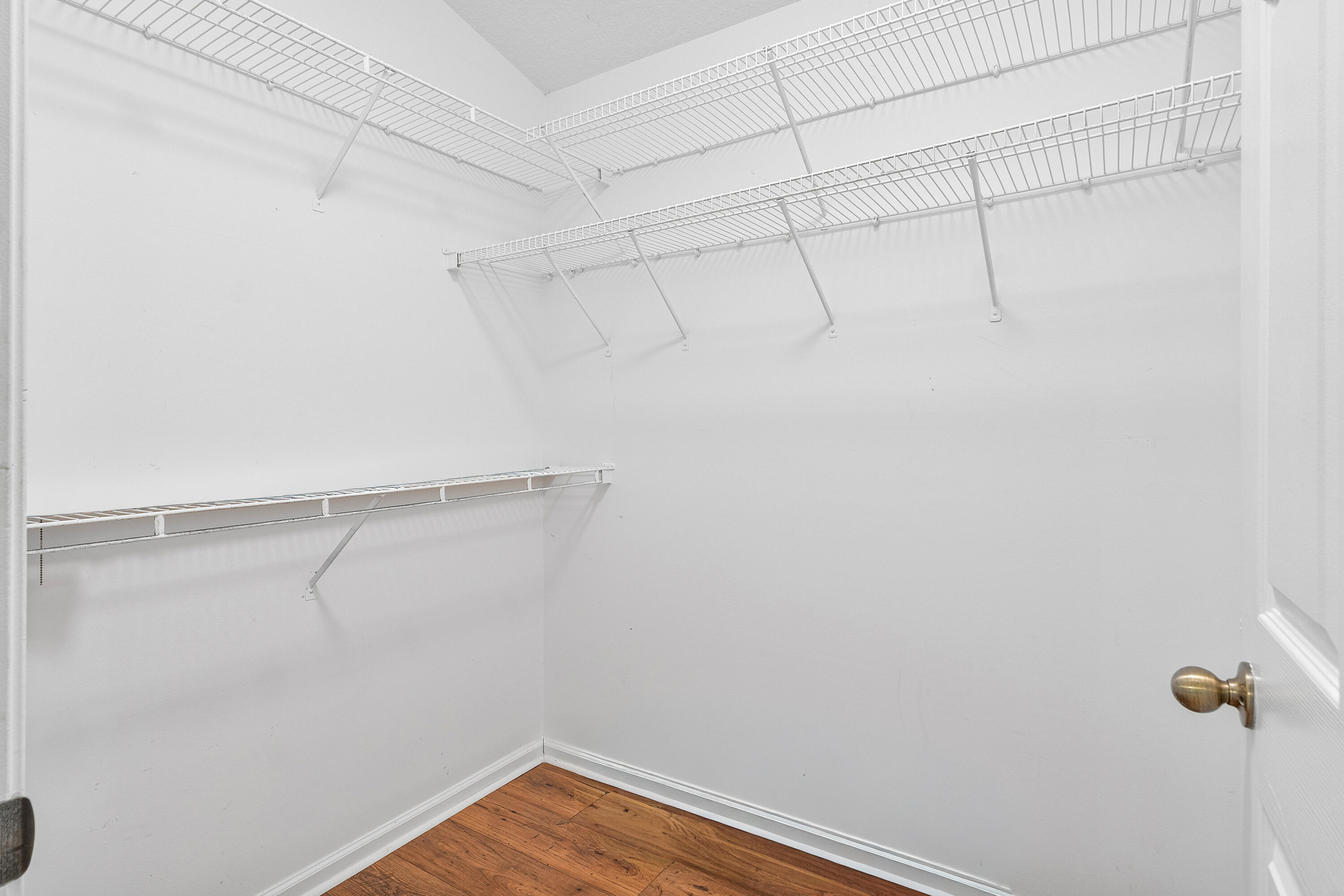 Storage area featuring wood-finish flooring and tiered white wire shelving in primary bedroom one.