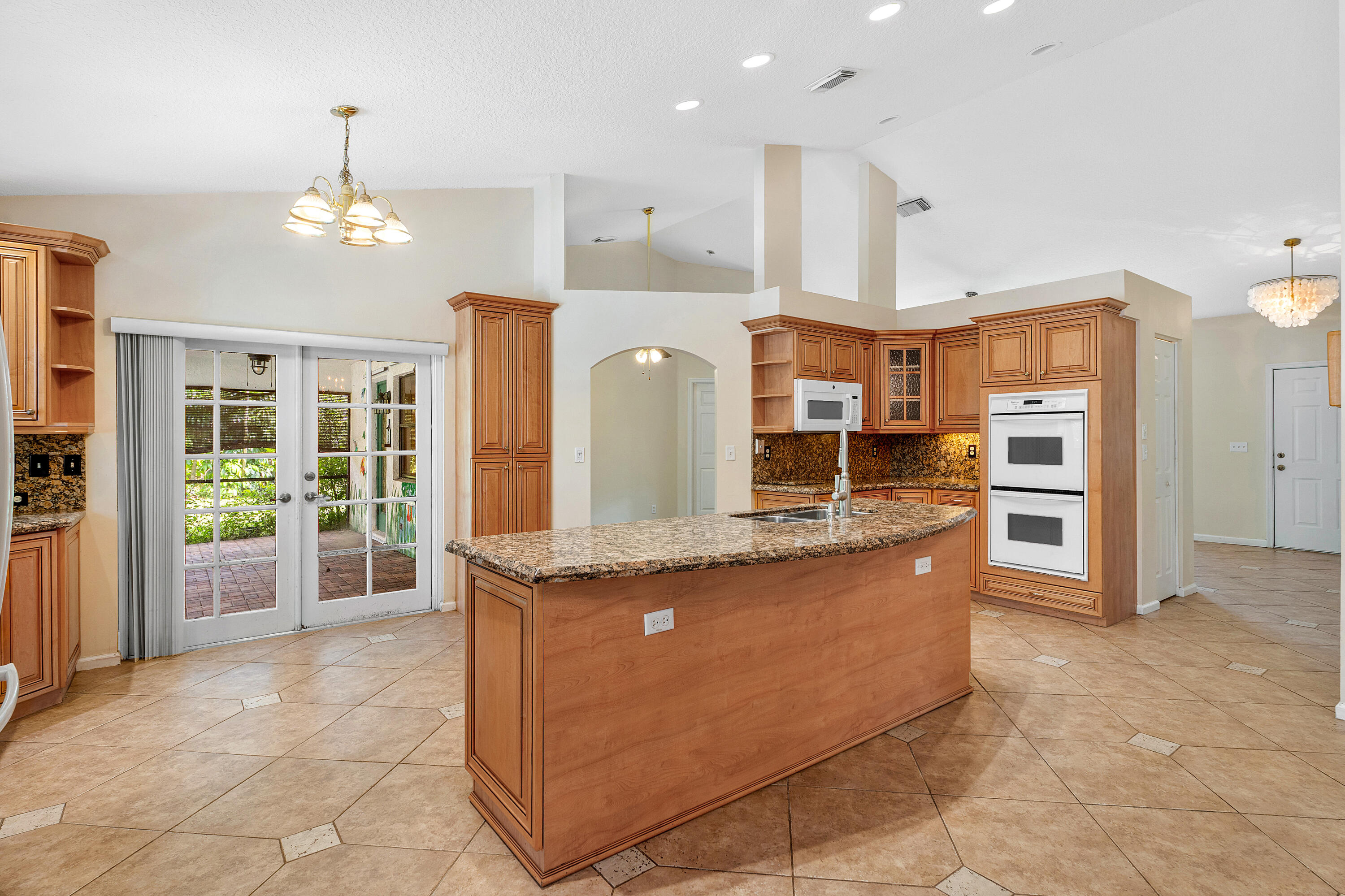 Kitchen featuring wood cabinetry, a stone-surfaced center island, double wall ovens, vaulted ceilings, and tile flooring