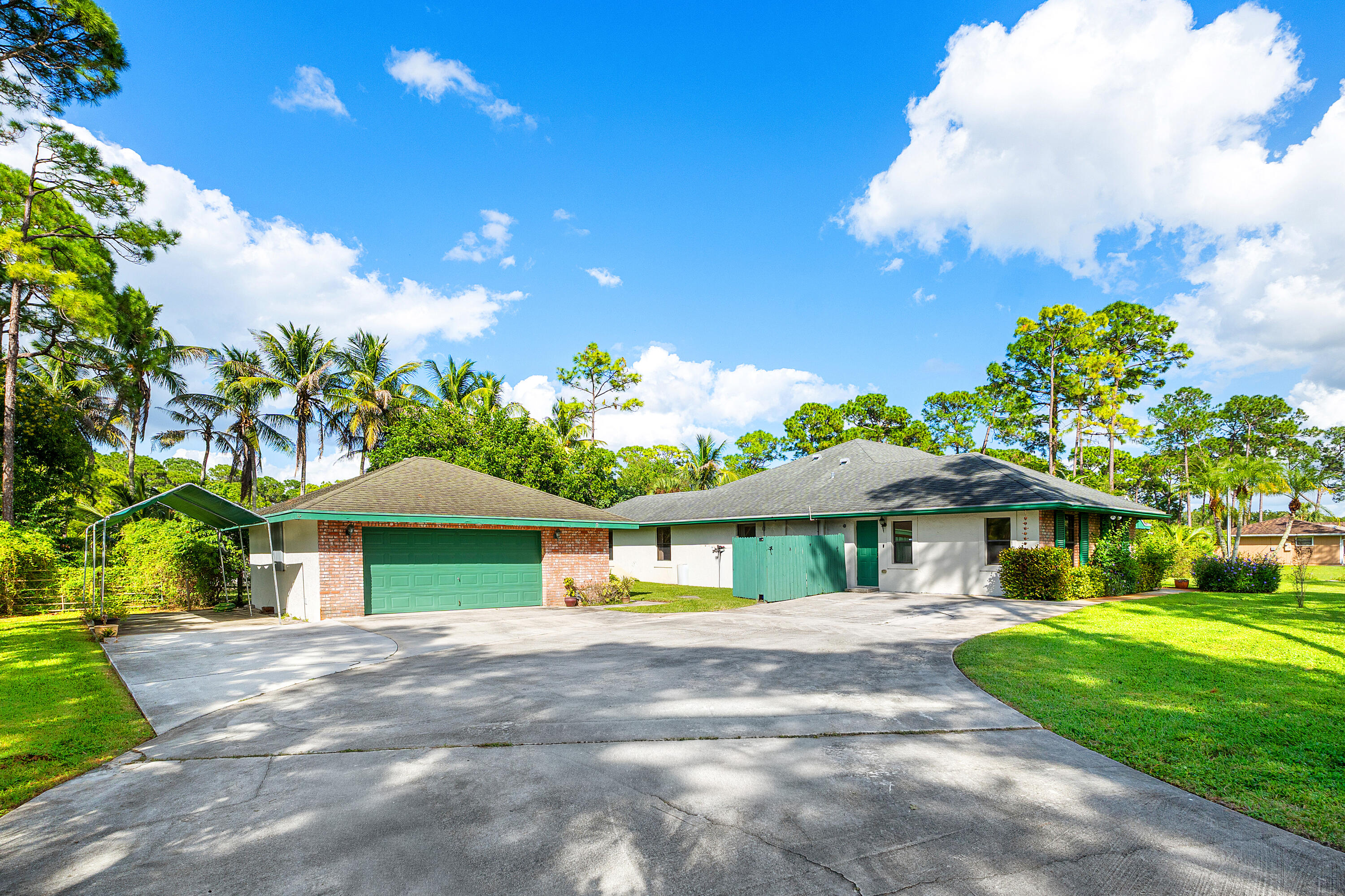 Exterior featuring a detached 2.5 car-garage with an attached carport, brick veneer detailing, a concrete driveway, and expansive lawn space Exterior featuring a detached 2.5 car-garage with an attached carport, brick veneer detailing, a concrete driveway, and expansive lawn space