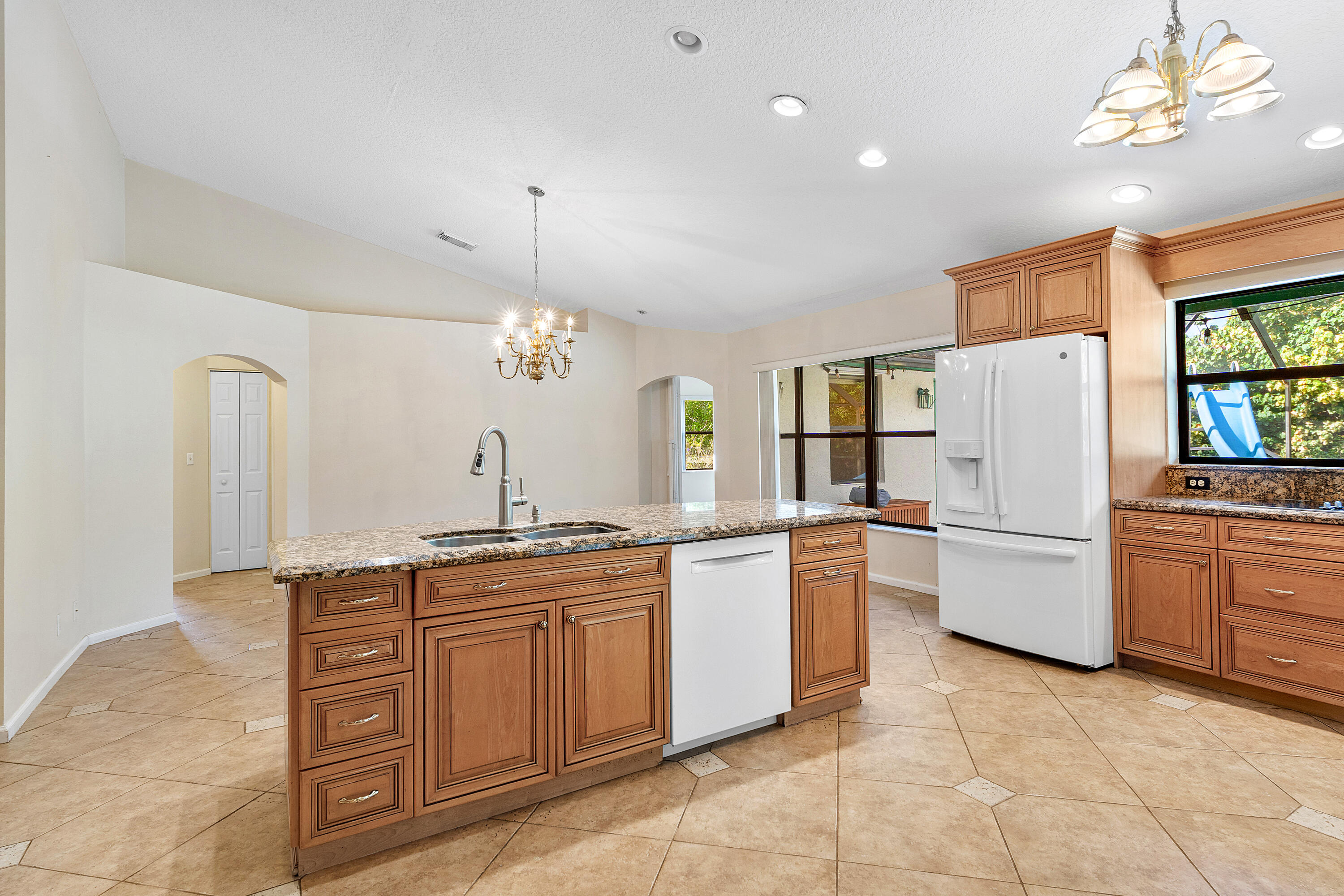 Kitchen featuring wood cabinetry, stone countertops, central island with integrated sink, ceramic tile flooring, and recessed lighting
