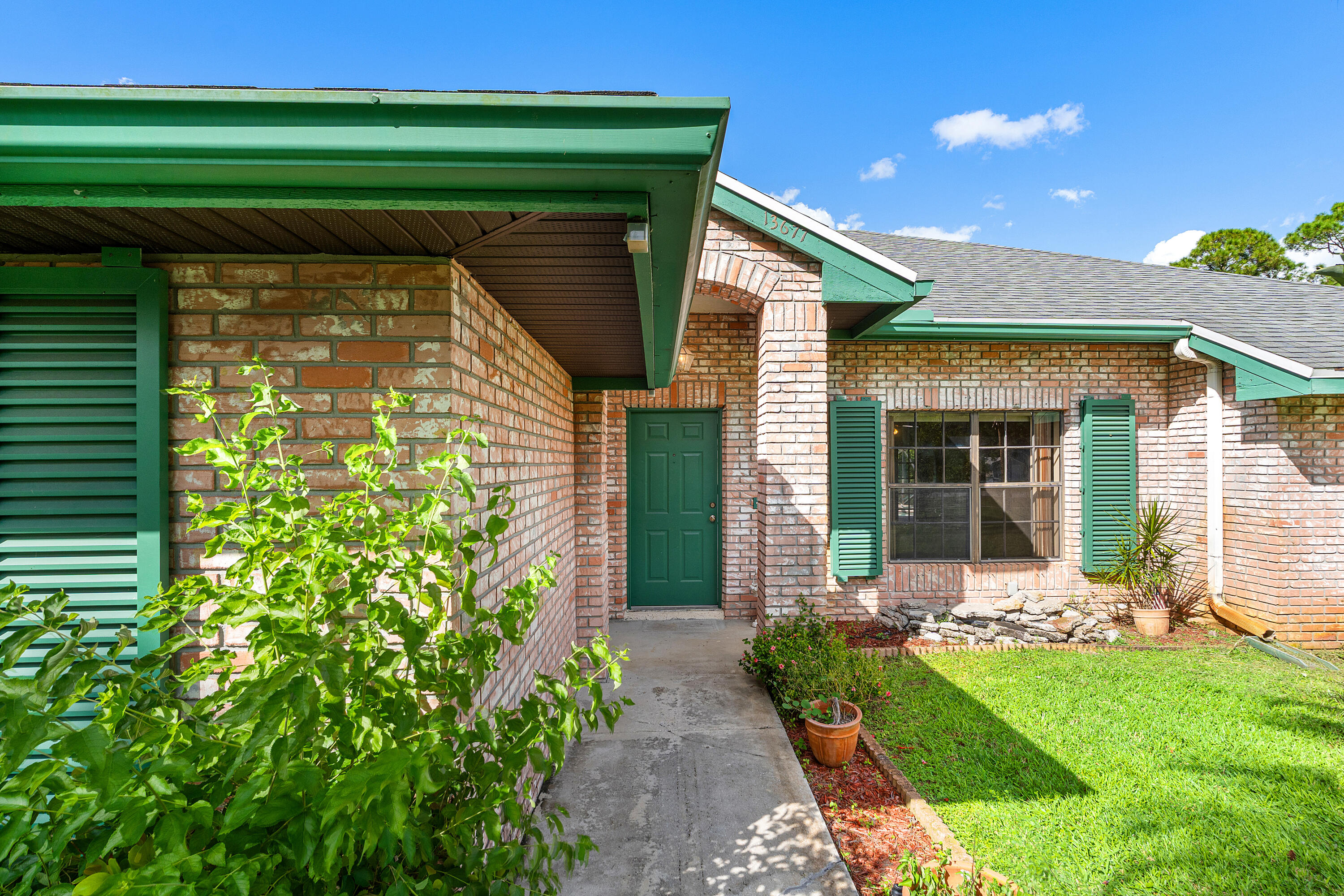 Brick exterior featuring a recessed entry, arched masonry detail, green louvered shutters, and a concrete walkway Brick exterior featuring a recessed entry, arched masonry detail, green louvered shutters, and a concrete walkway