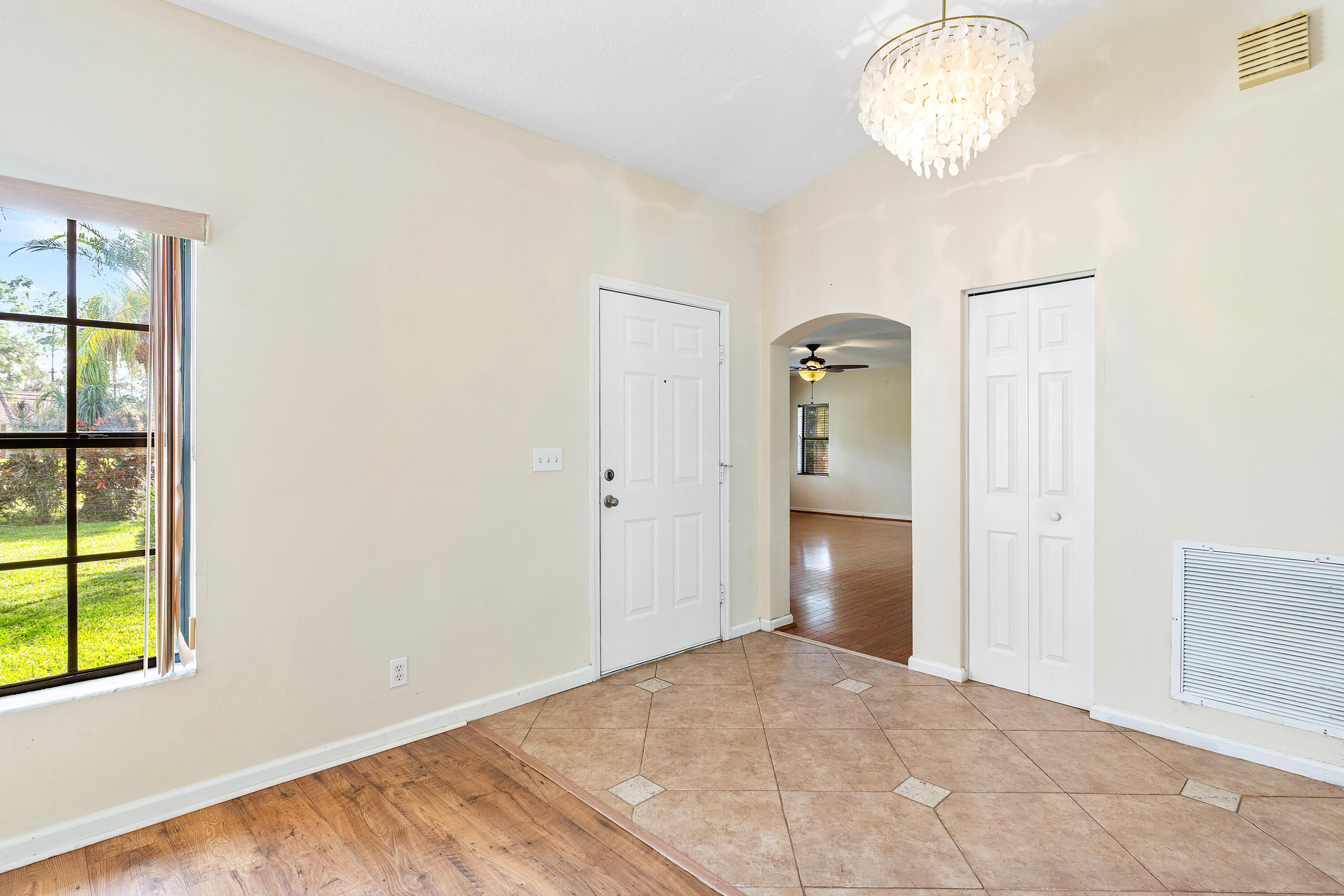 Foyer featuring vaulted ceilings, decorative tiered chandelier, tile flooring with inset accents, multi-pane window, and wood-finish flooring