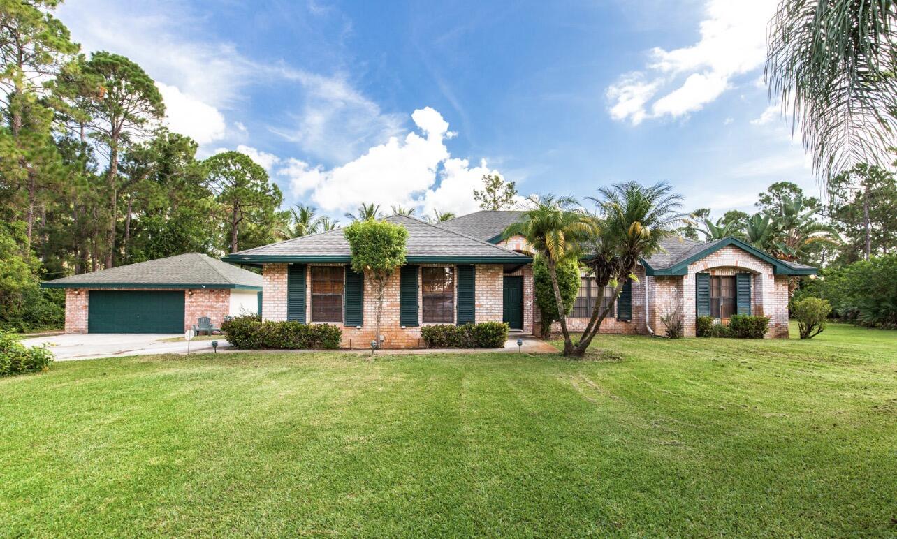 Single-story residence featuring a brick facade, detached 2.5 car garage, expansive lawn, and mature palm trees