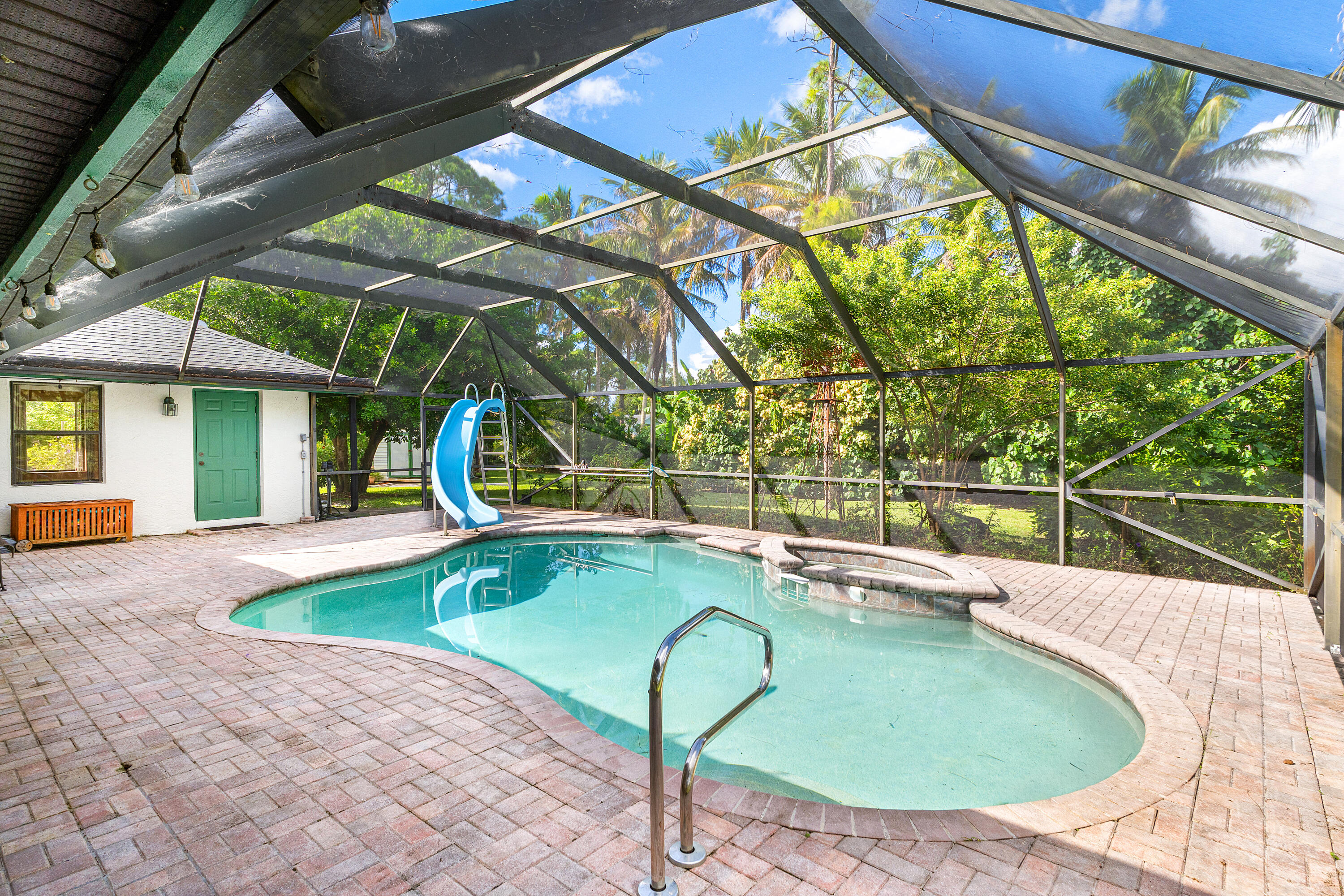 Screen-enclosed patio featuring a paver deck, swimming pool with a built-in slide, and an integrated spa