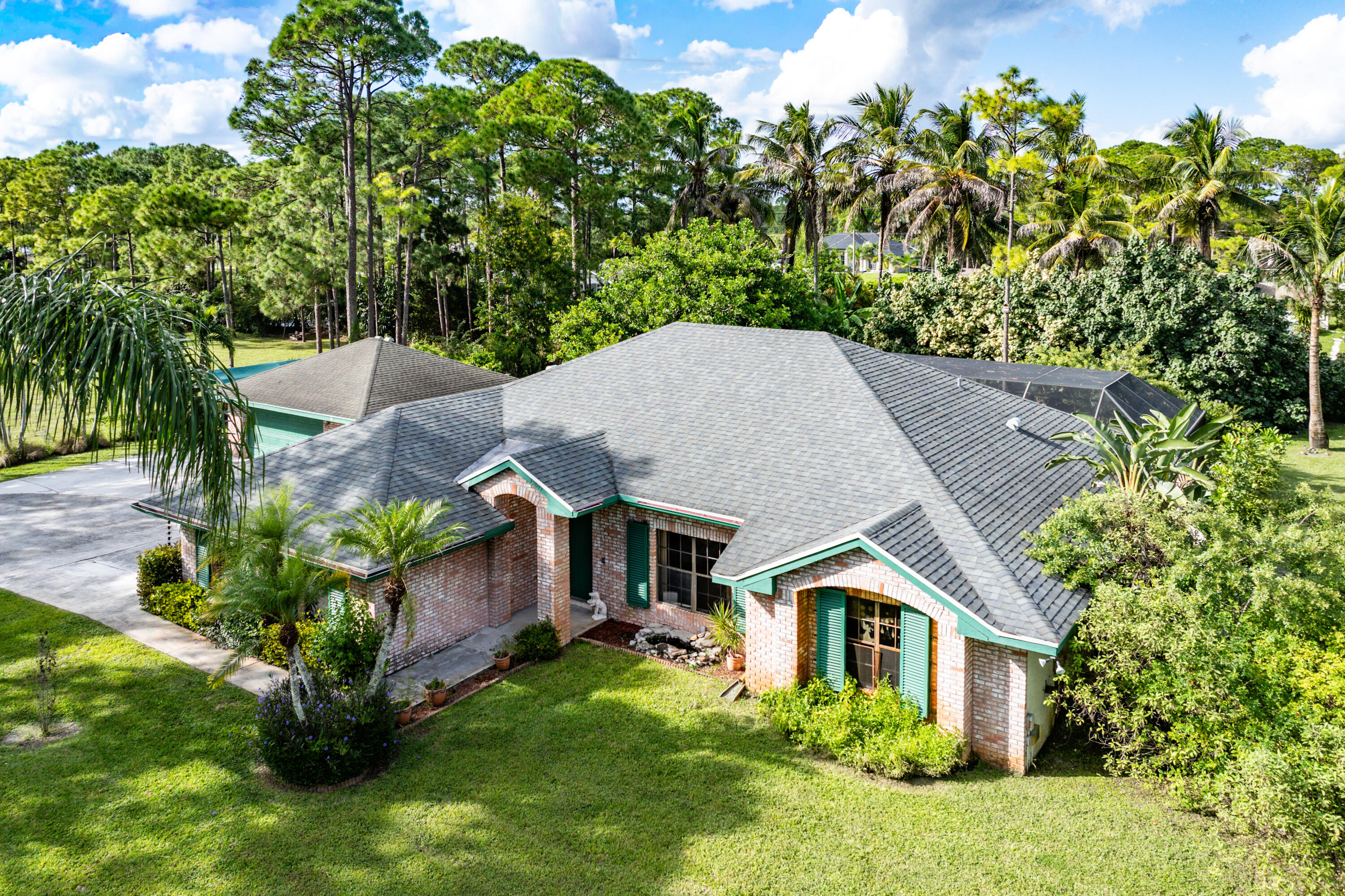 Single-story brick exterior featuring a multi-gabled asphalt shingle roof, attached garage, and decorative shutters on a lot with mature landscaping