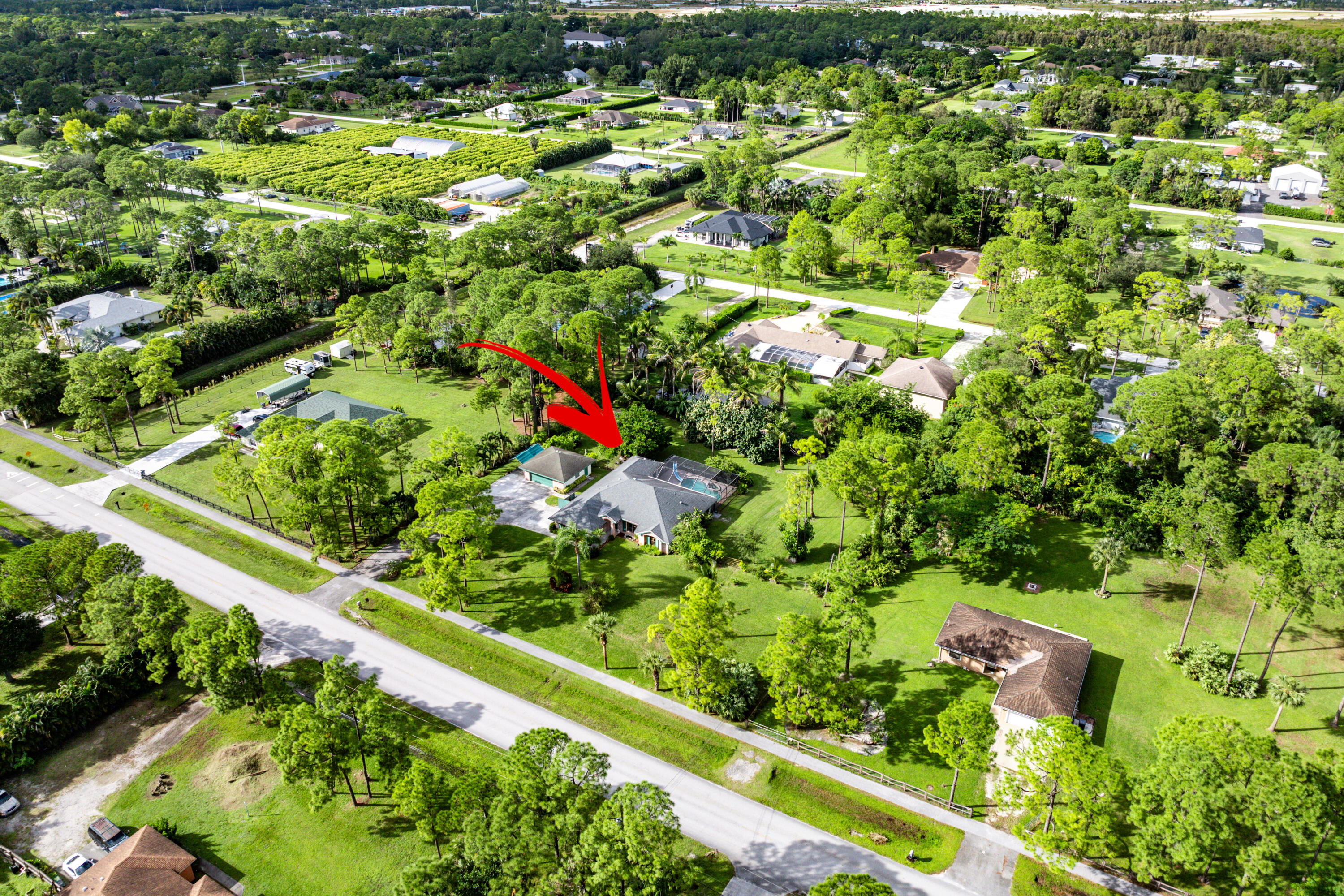 Aerial perspective of a detached residence featuring a screened-in pool enclosure, concrete driveway, and expansive grass lot with mature trees