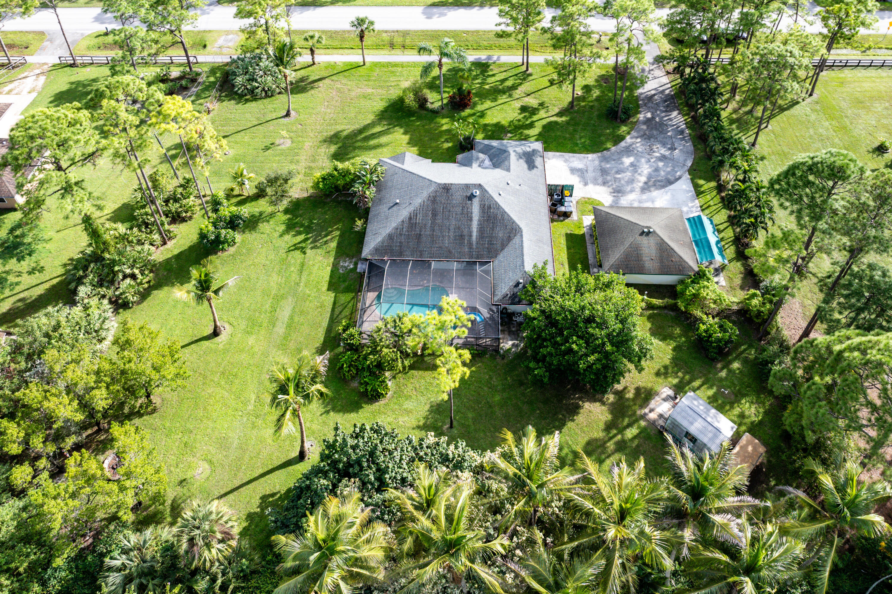 Aerial perspective of a sprawling parcel featuring a multi-structure property, a screened-in swimming pool, a detached garage, and mature landscaping