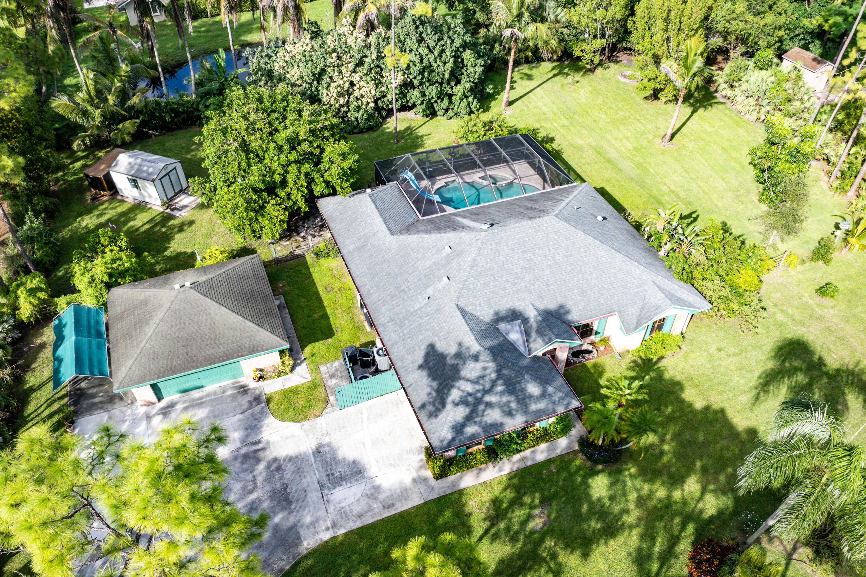 Aerial perspective of a property featuring an expansive lawn, a detached storage structure, a screen-enclosed pool, and a paved driveway
