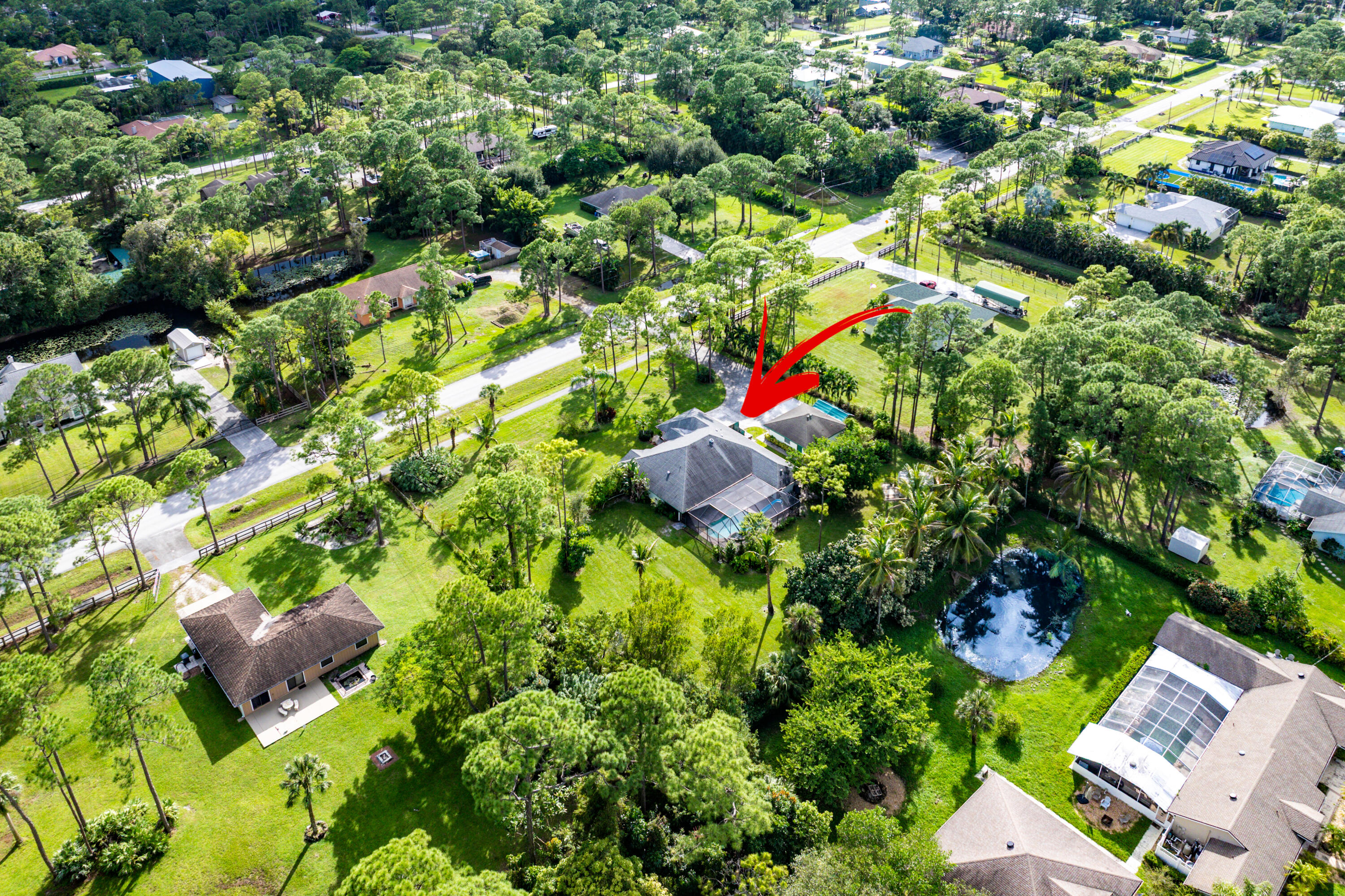Aerial perspective of a detached residence featuring a multi-slope roof, an attached garage, a screen-enclosed pool, and a private driveway situated on a wooded lot