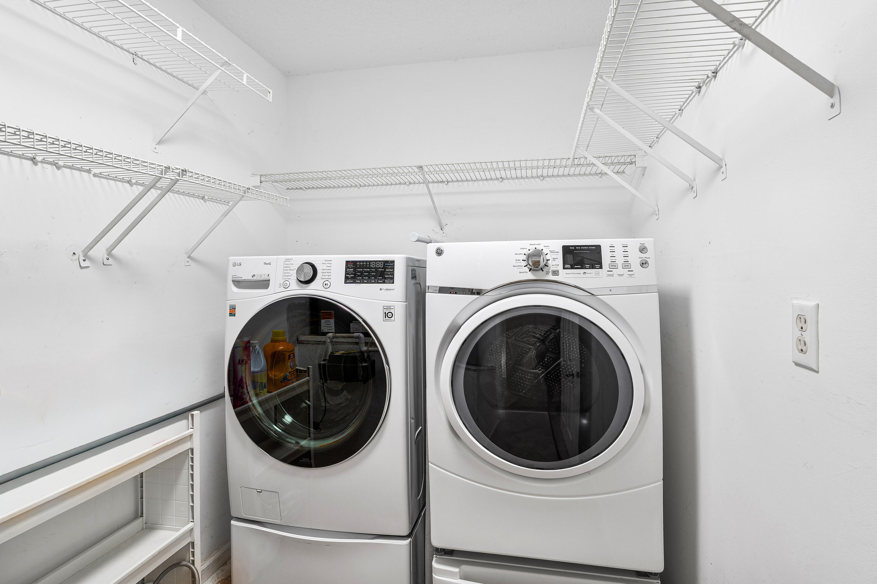 Laundry room featuring new white appliances, integrated pedestals, and multi-level wire shelving