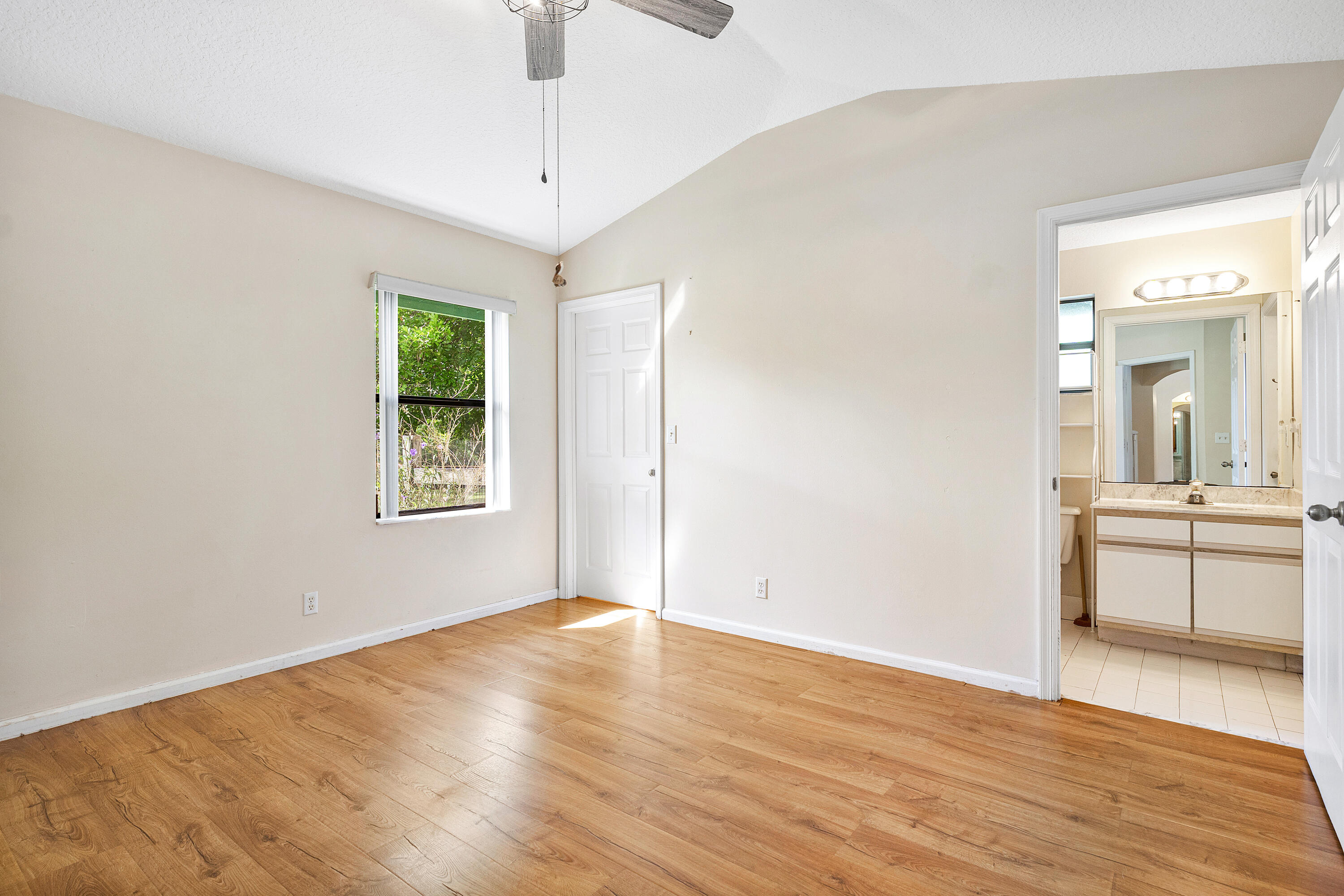 Primary bedroom ensuite number two featuring wood-finish flooring, vaulted ceilings, a ceiling fan, and a single window