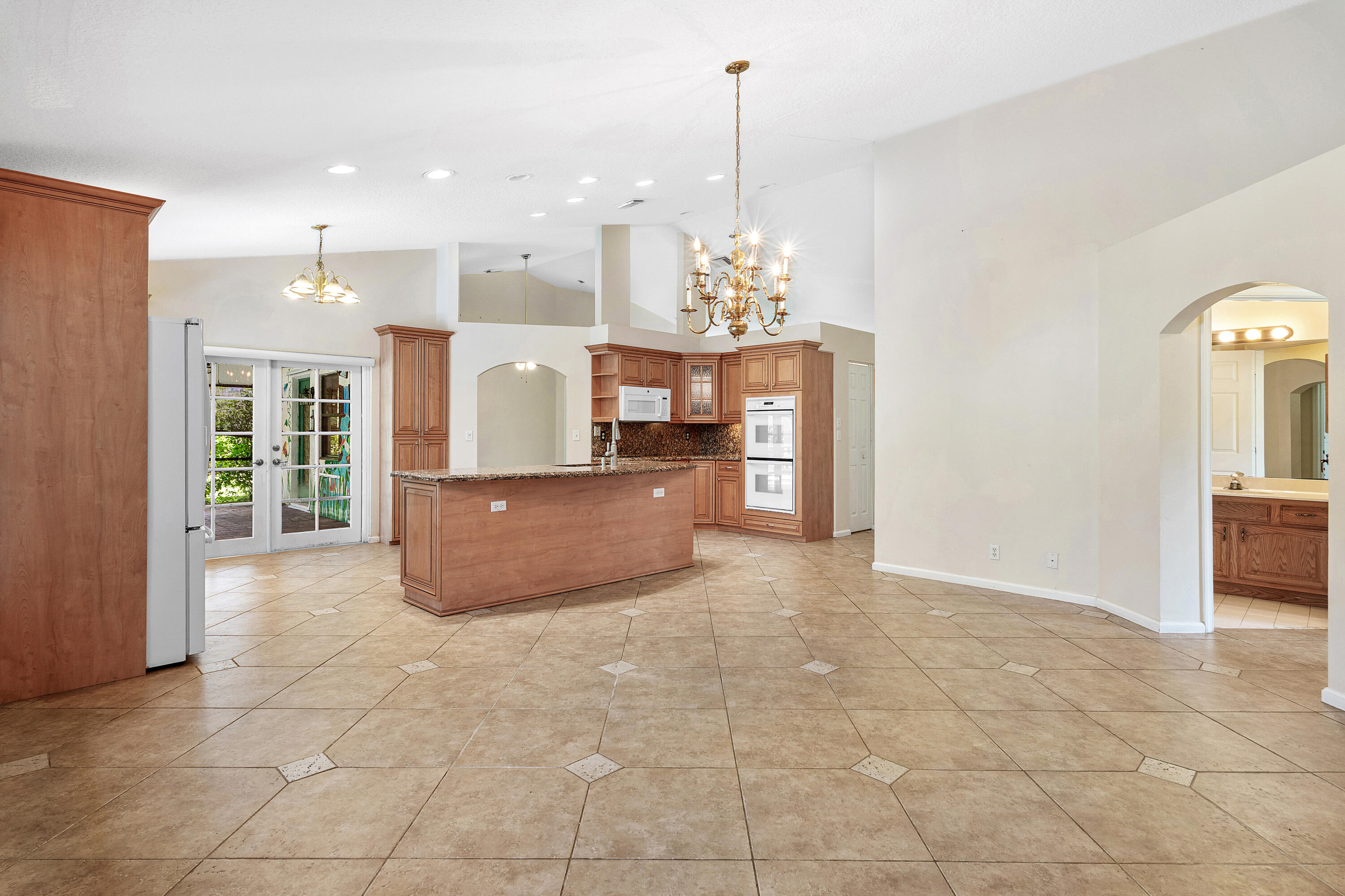 Open-concept interior featuring vaulted ceilings, tile flooring with decorative inserts, a kitchen island, recessed lighting, and ornate chandeliers