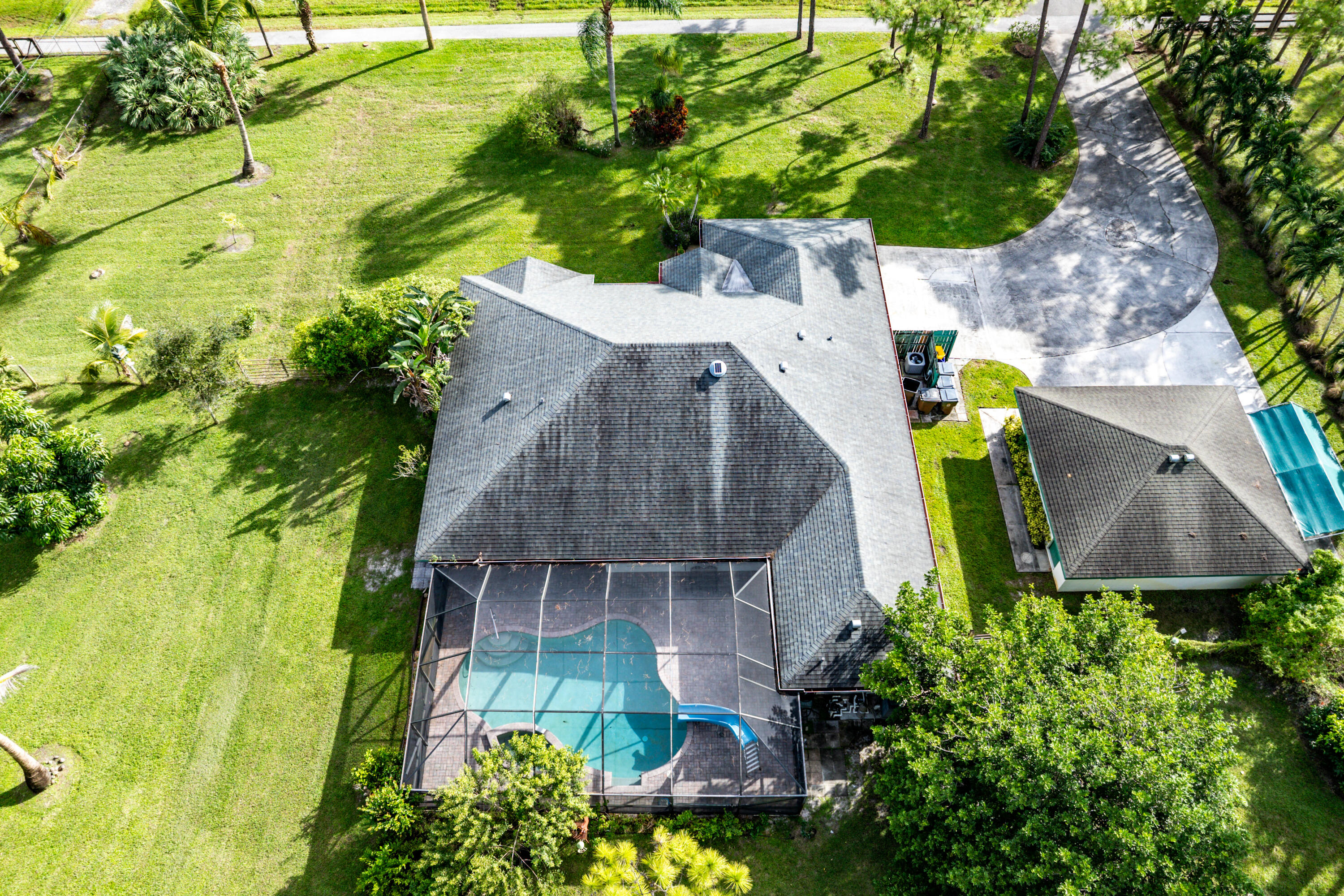 Aerial view of a property featuring an expansive manicured lawn, a detached garage, a paved circular driveway, and a screened-in swimming pool with an integrated slide