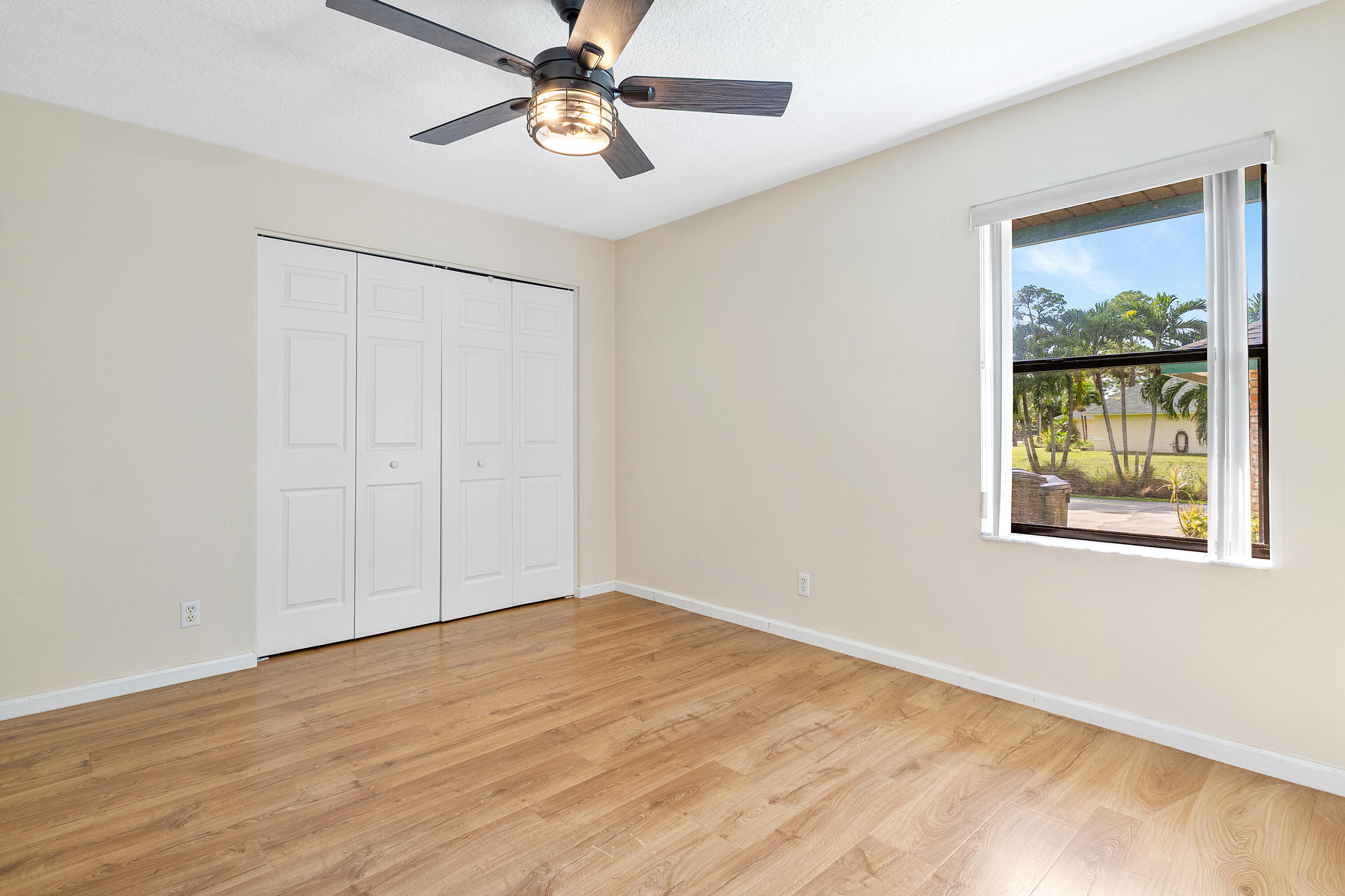 Bedroom three featuring wood-finish flooring, a multi-panel closet with white doors, and a ceiling fan with integrated lighting