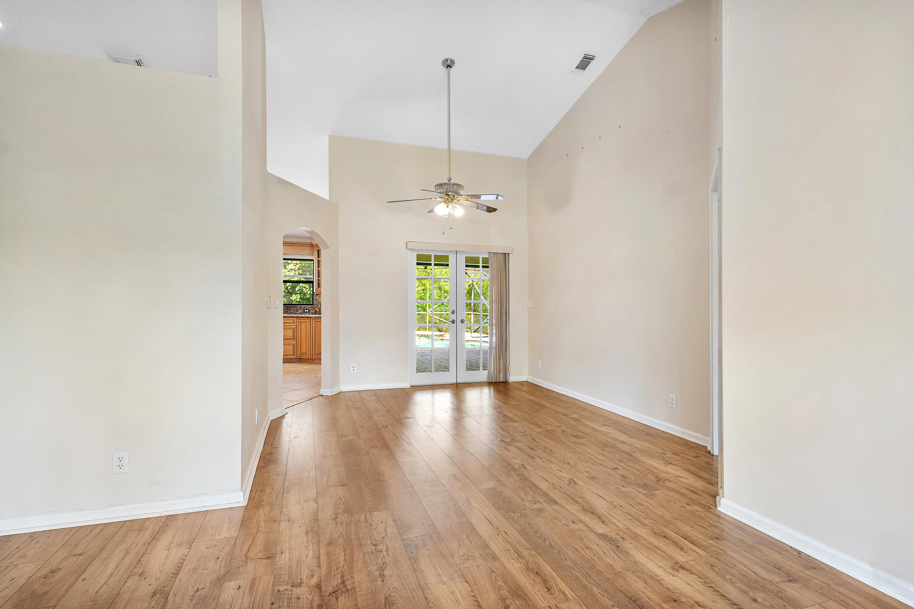 Vaulted ceilings featuring a central ceiling fan, wood-finish flooring, and glass-paned French doors