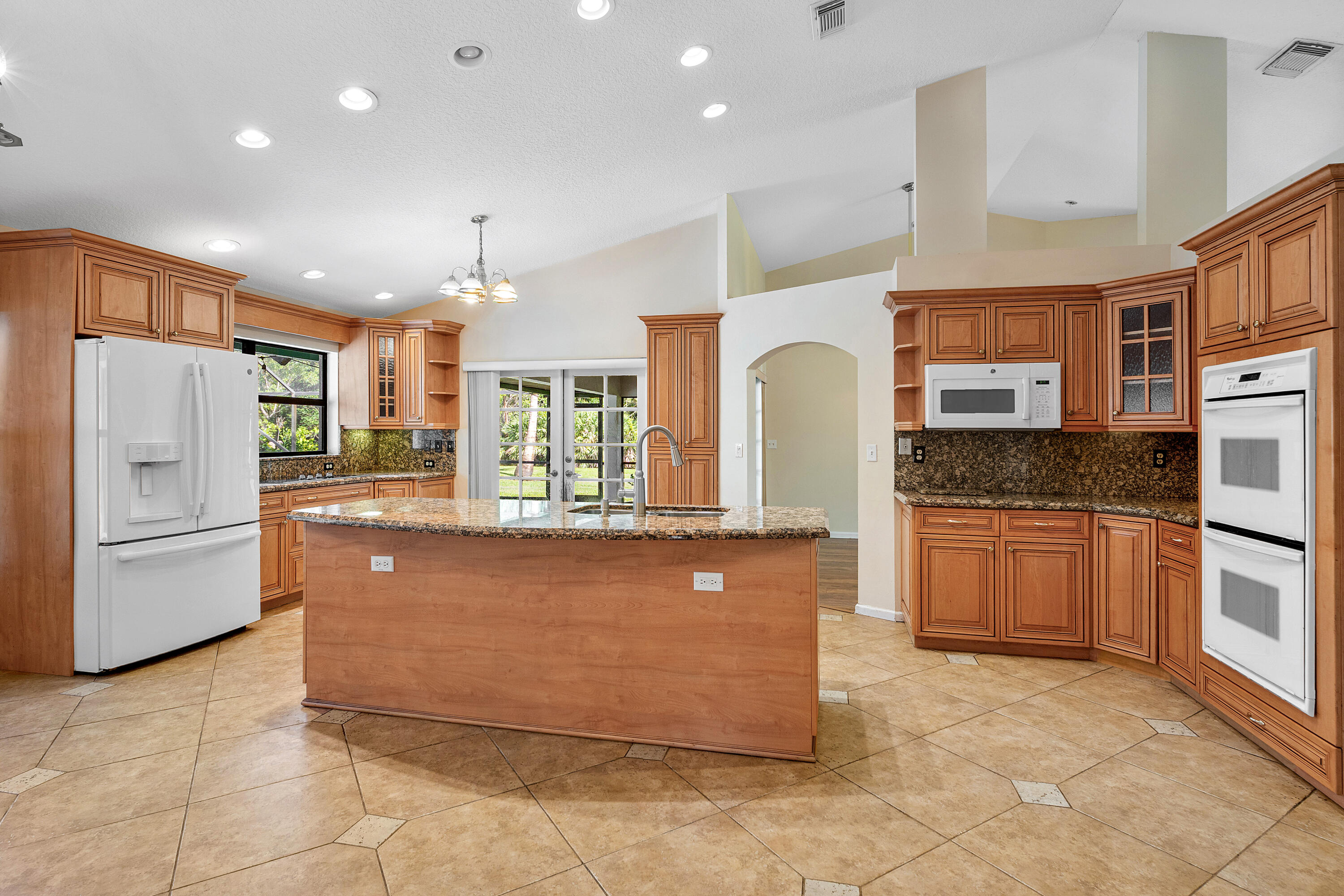 Kitchen featuring custom wood cabinetry, stone countertops, central island with sink, built-in double wall oven, and tile flooring