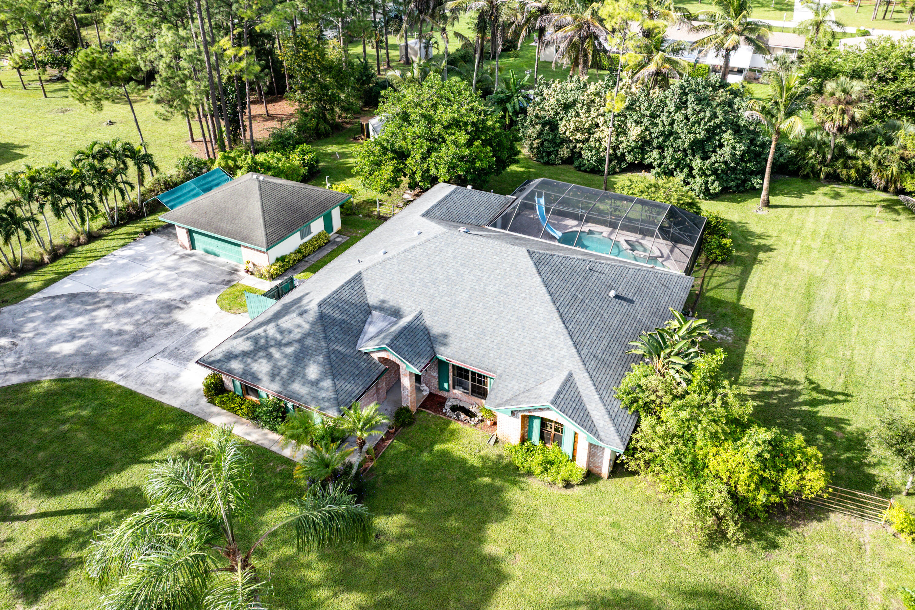 Aerial perspective featuring a shingled roof residence with a detached garage, a screened-in pool enclosure, and expansive landscaped grounds
