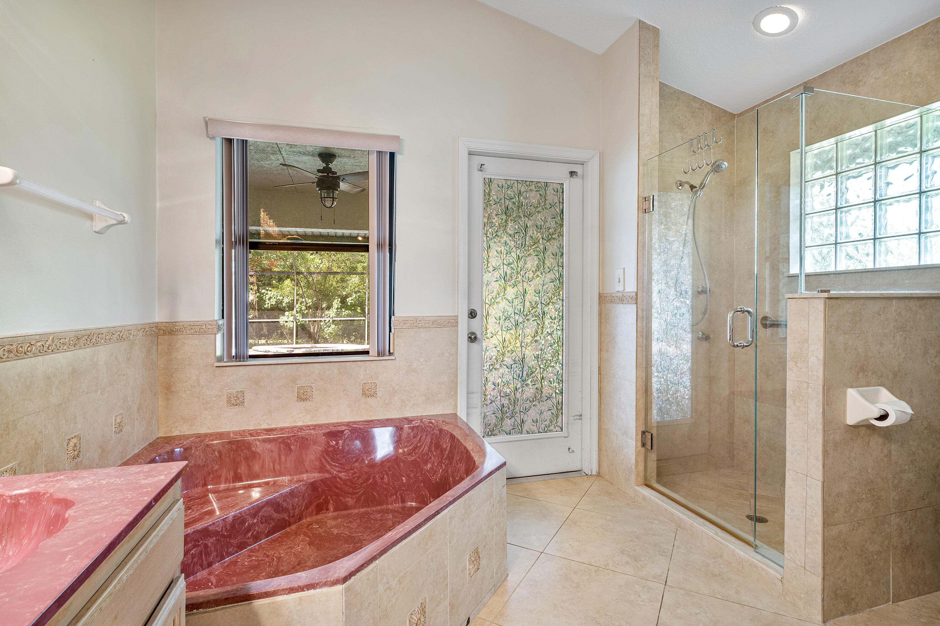 Primary bathroom ensuite number one featuring a custom built-in soaking tub, a glass-enclosed shower with tile surround, a frosted glass exterior door, ceramic tile flooring, and a glass block window