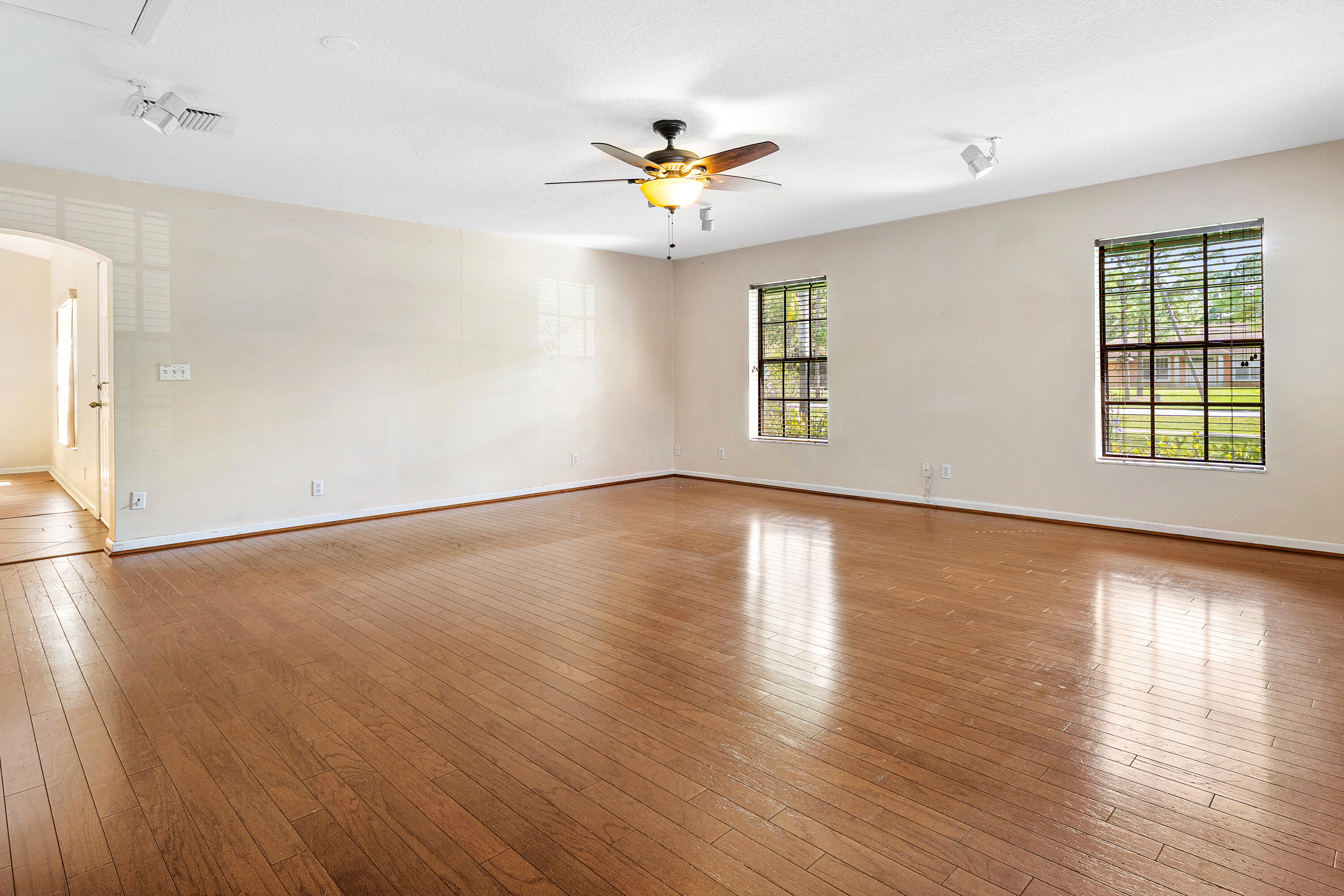 Wood-finish flooring throughout, dual windows with grid muntins, a ceiling fan with integrated lighting, and recessed track lighting