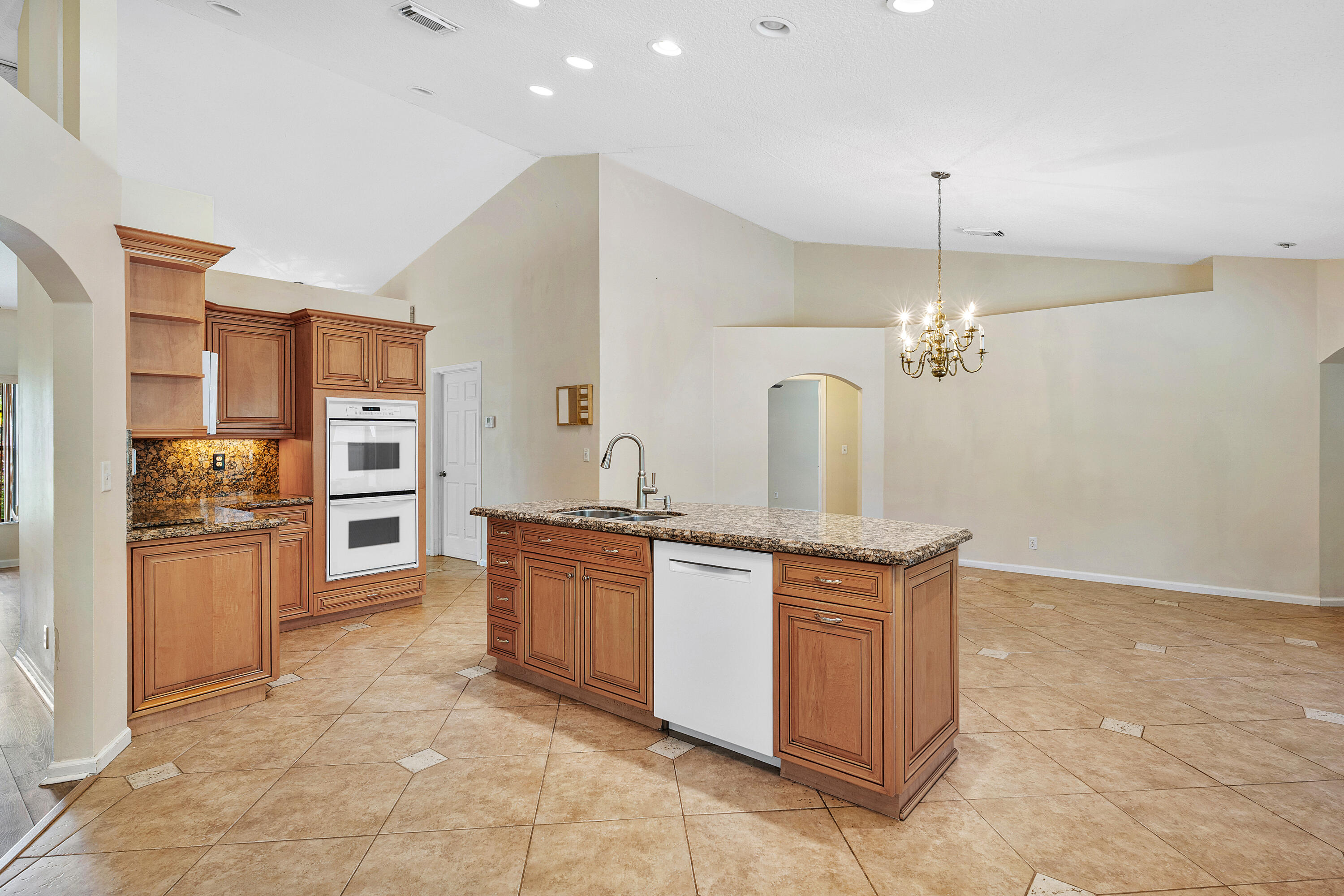 Kitchen featuring raised-panel wood cabinetry, stone countertops, double wall ovens, a center island with integrated dishwasher, and tile flooring throughout