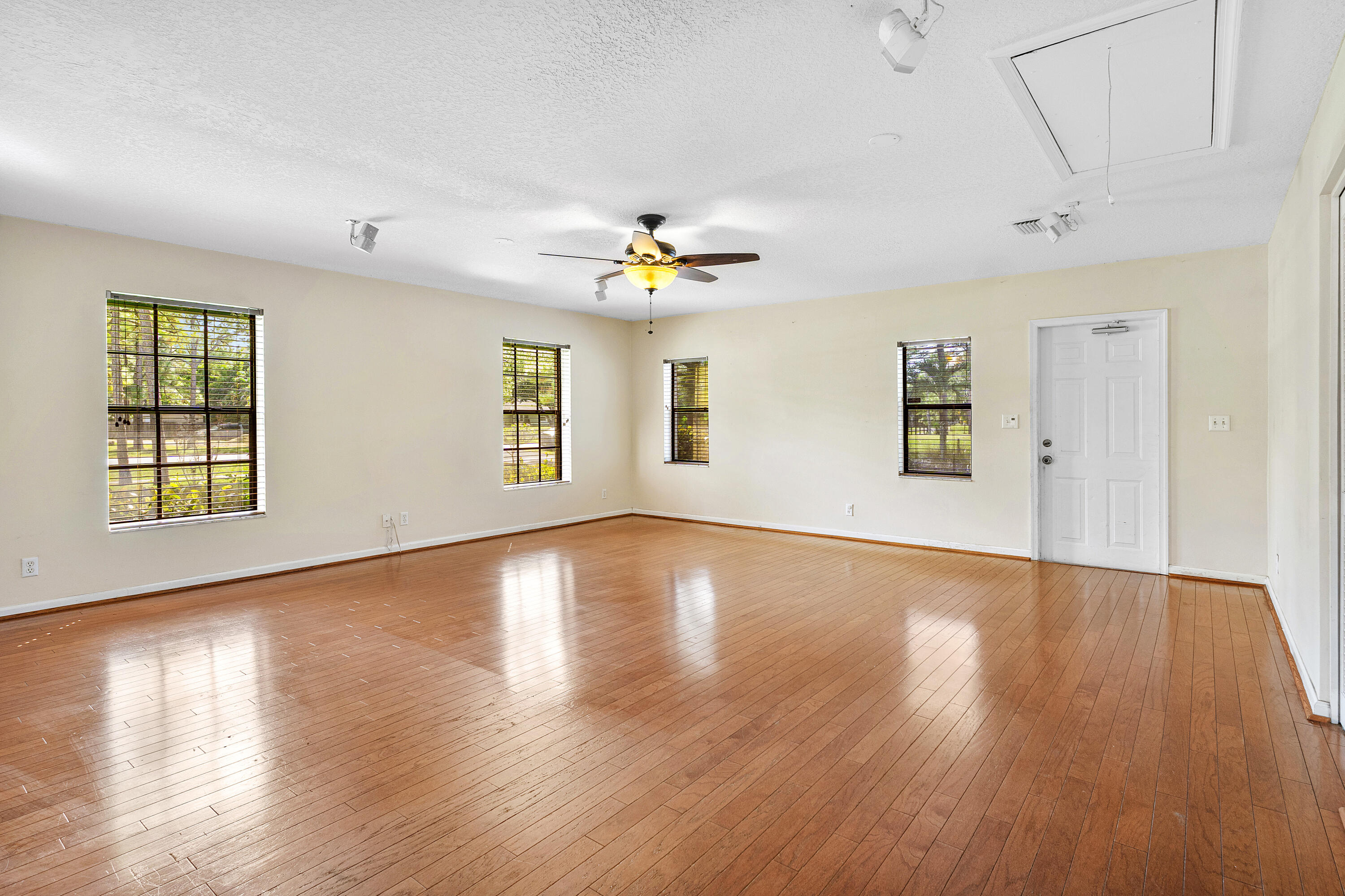 Open interior space featuring wood-finish flooring, recessed lighting, a ceiling fan with integrated light fixture, multiple windows with grid detailing, and a panel door with exterior access
