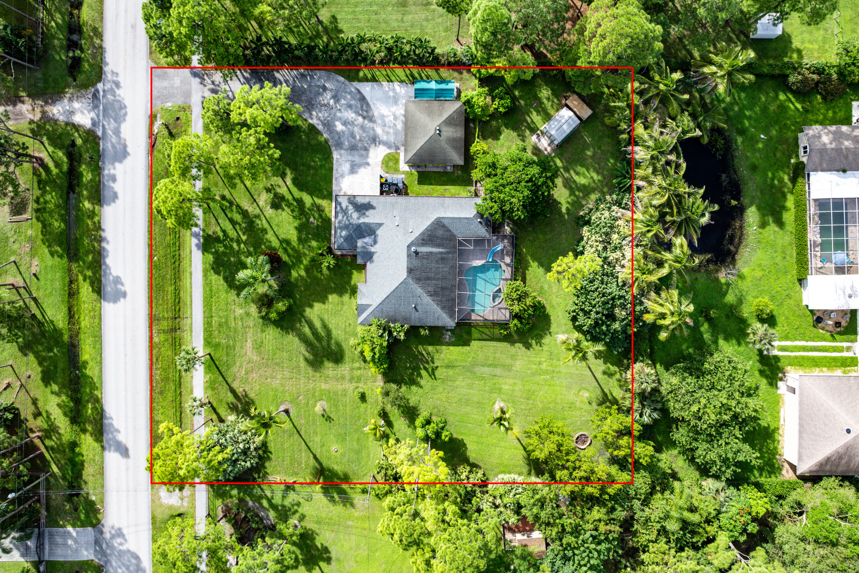 Aerial perspective of a sprawling lot featuring a multi-gabled residence, a screened-in pool, a detached storage structure, and expansive green space with mature landscaping