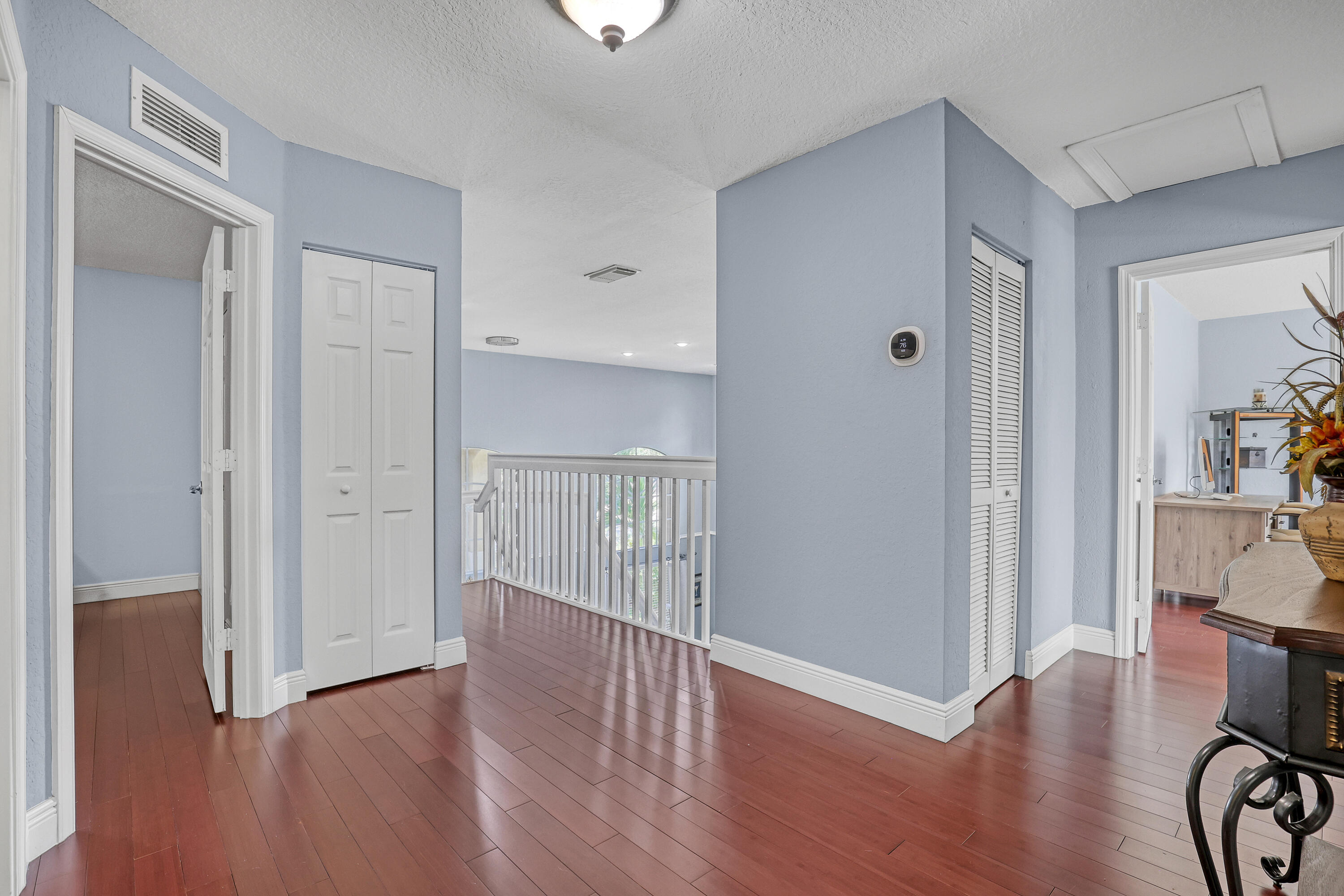 Wood-finish flooring, white railing with vertical balusters, dual louvered closet doors, and a ceiling-mounted light fixture