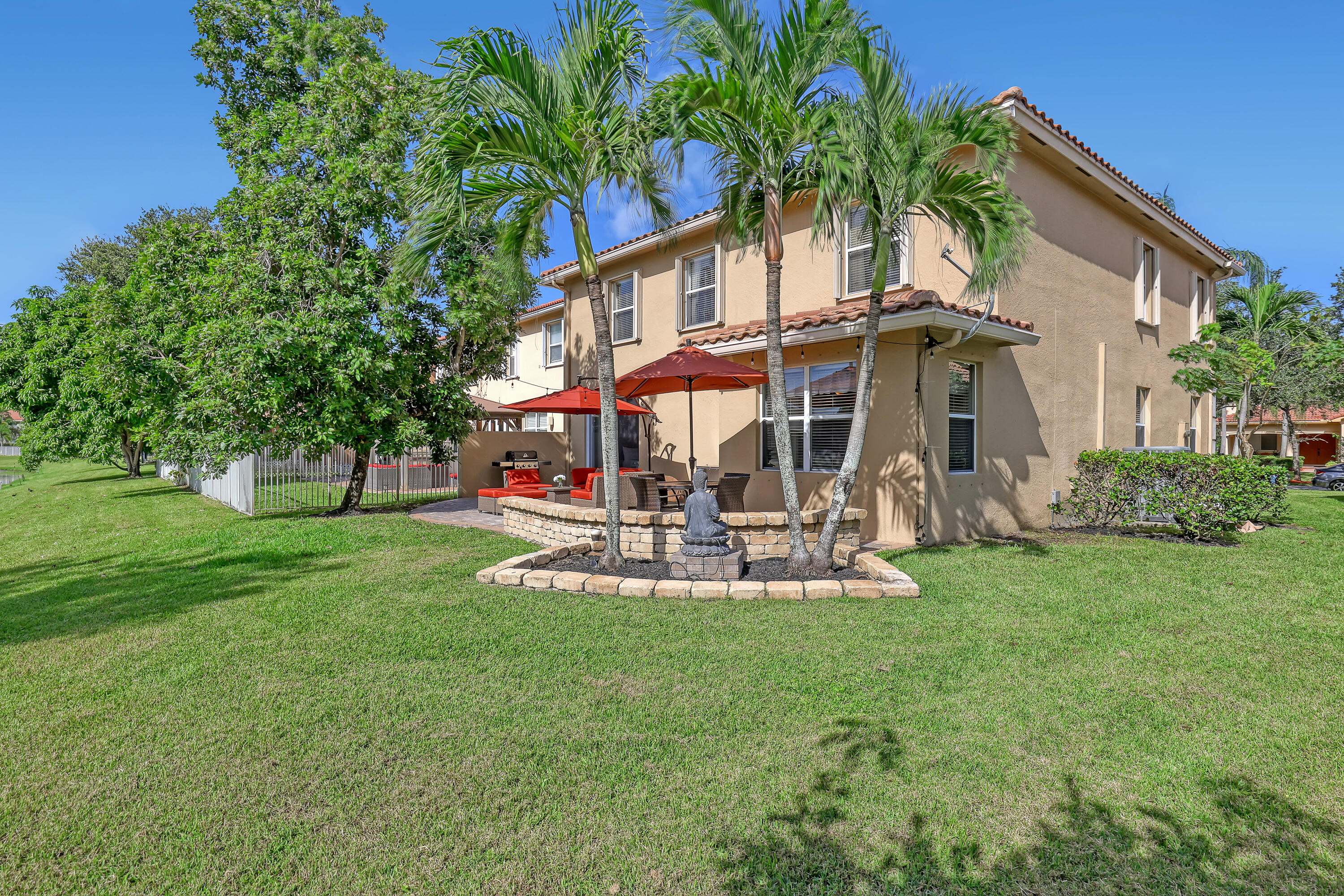 Rear exterior featuring a two-story stucco facade, tiled roof, paver patio, and decorative stone retaining wall with integrated palm trees