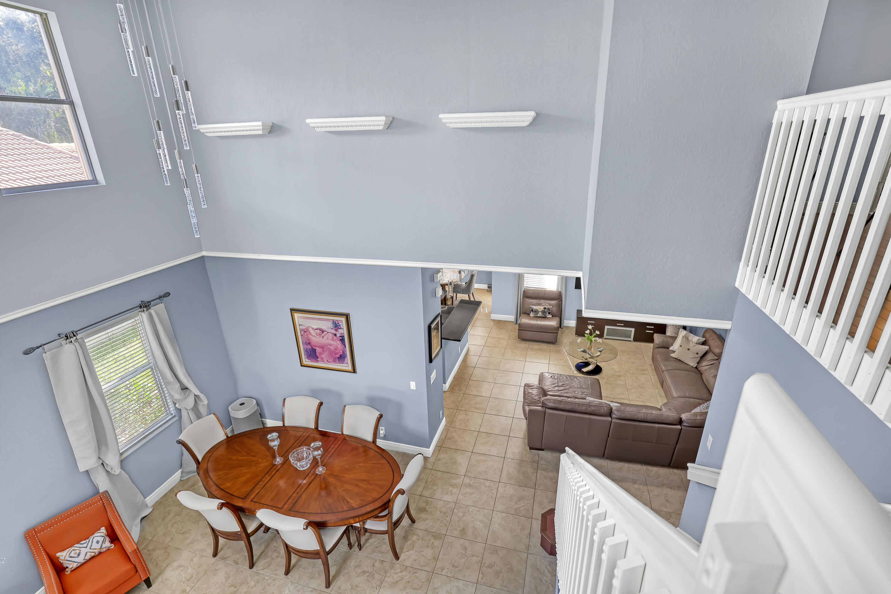 Double-height ceiling, tile flooring, upper-level landing with white balustrade, wall-mounted decorative ledges, and multi-pane window