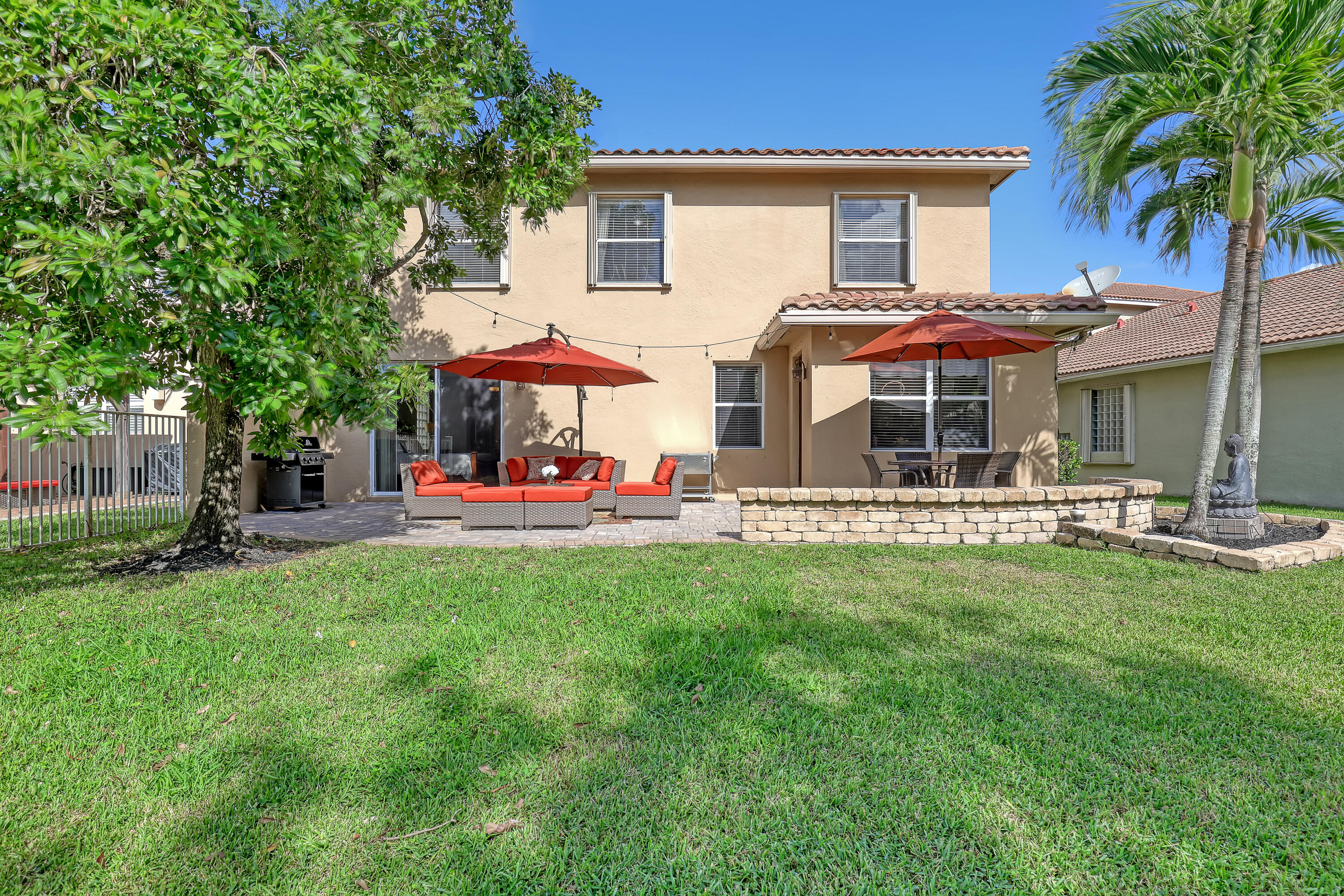Rear exterior featuring a stucco facade, tile roof, stone paver patio, and a tiered stone retaining wall