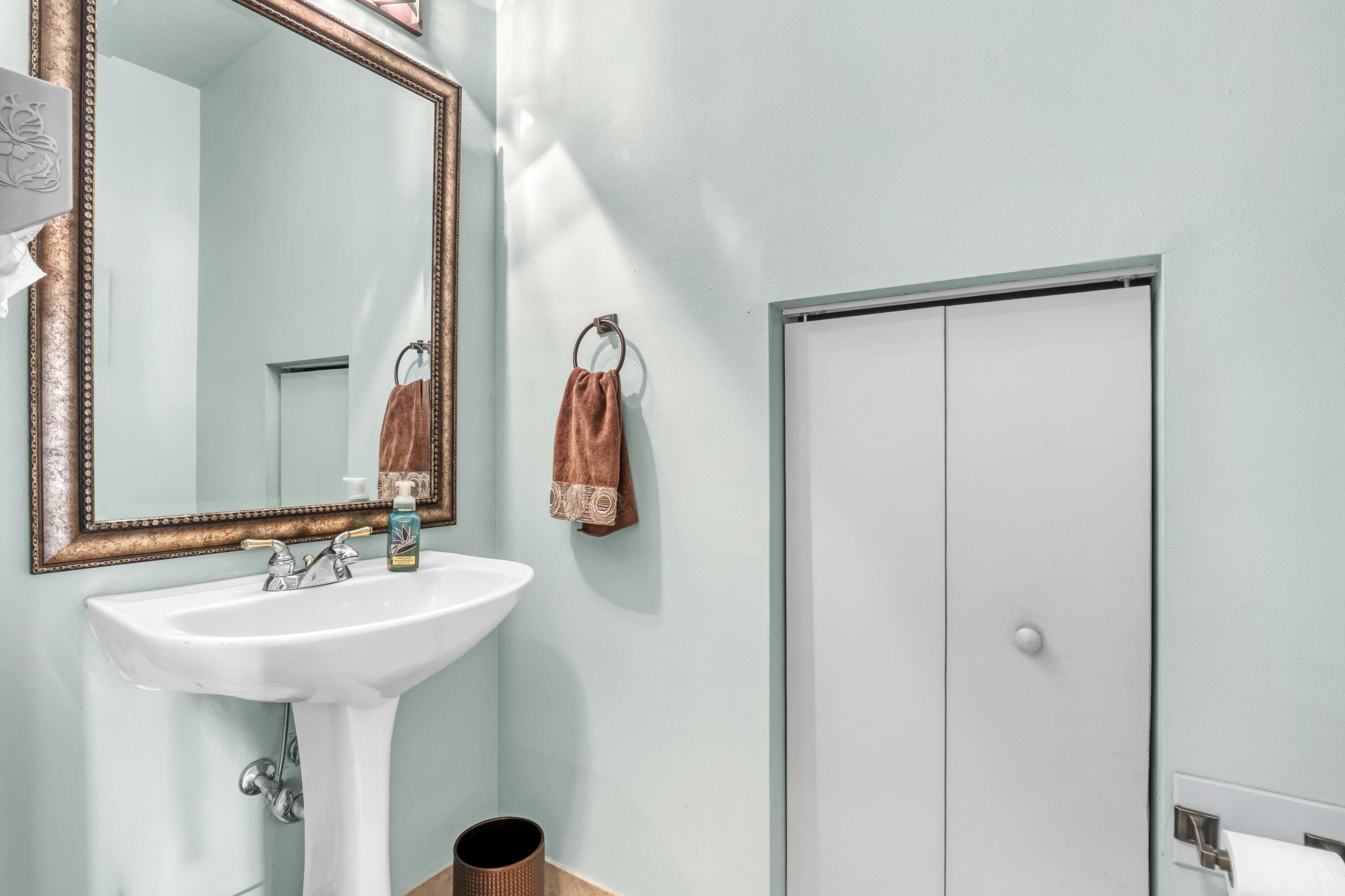 White pedestal sink with a metallic dual-handle faucet and bi-fold closet doors