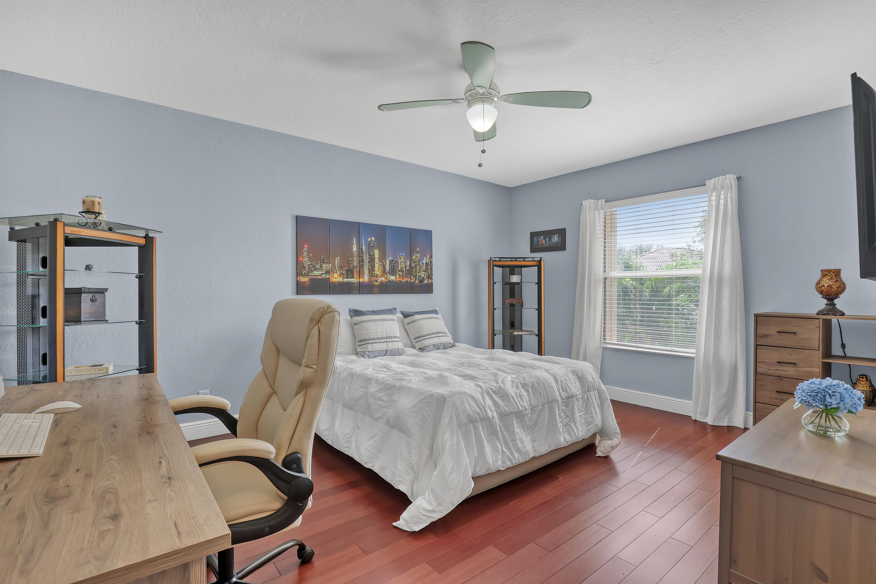Room featuring wood-finish flooring, a centrally mounted ceiling fan with integrated lighting, and a window with horizontal blinds