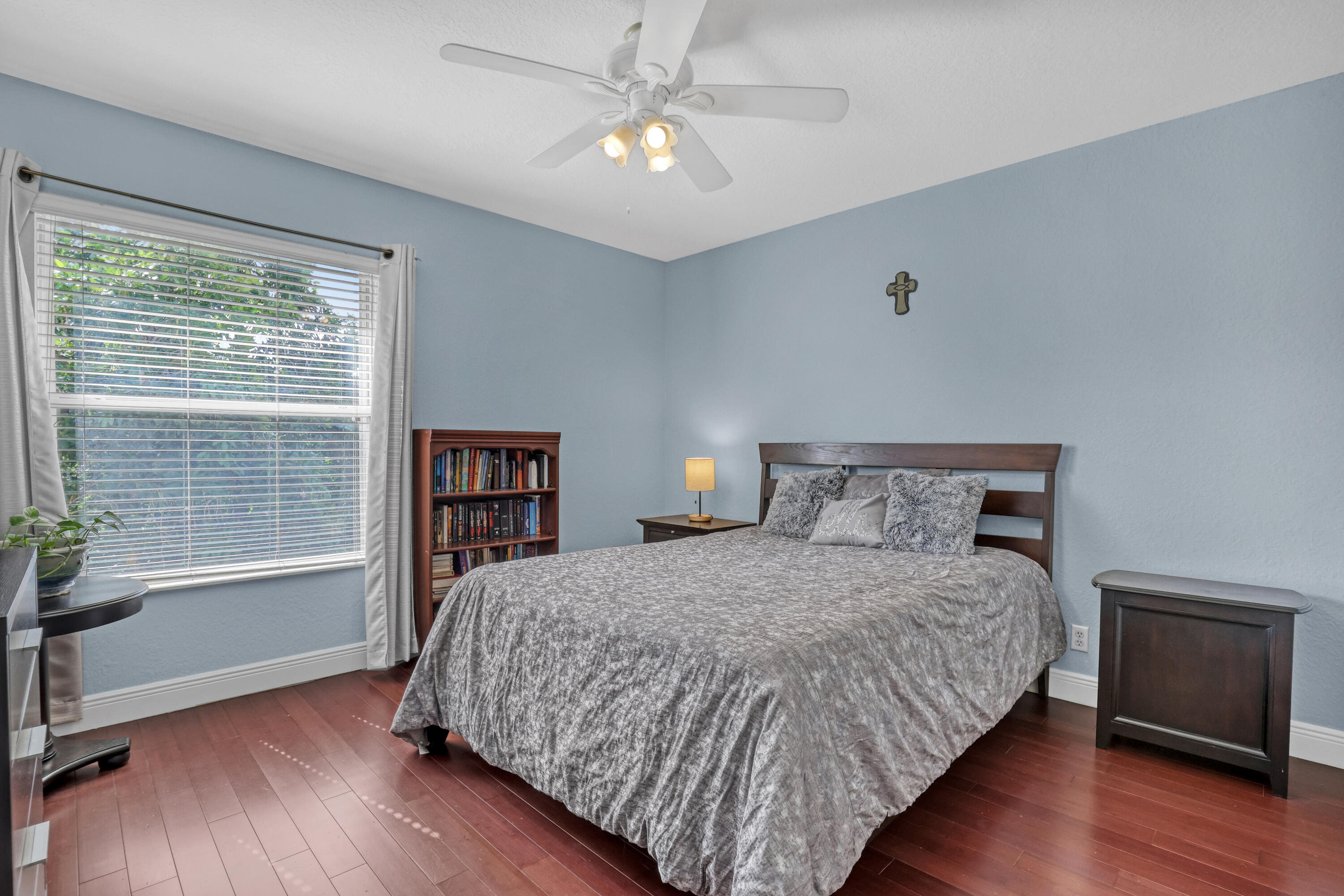 Bedroom featuring wood-finish flooring, a ceiling-mounted light fixture with fan, and a large window with horizontal blinds