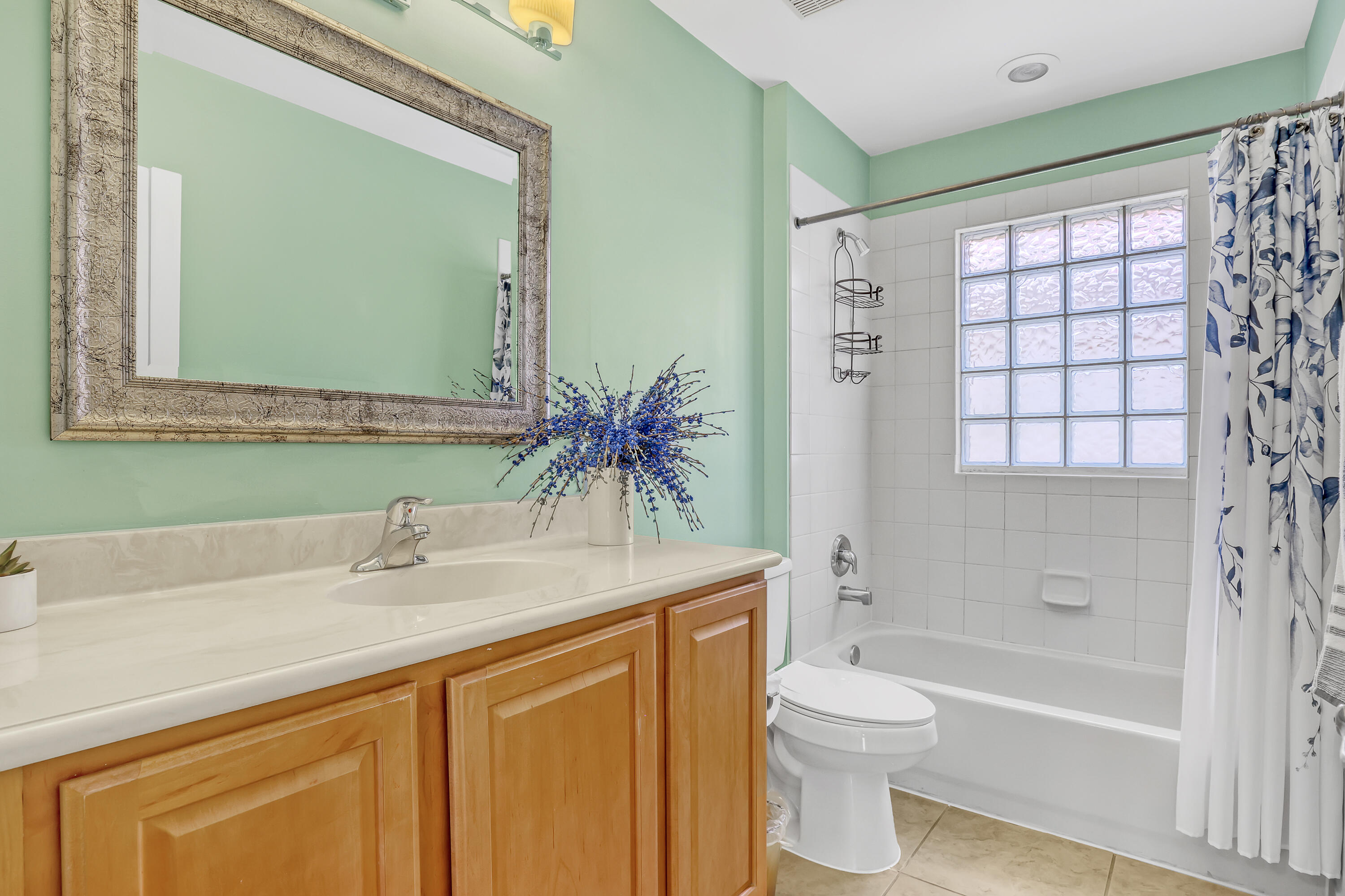Bathroom featuring a vanity with integrated sink and countertop, framed wall mirror, glass block window, and a tiled bathtub surround