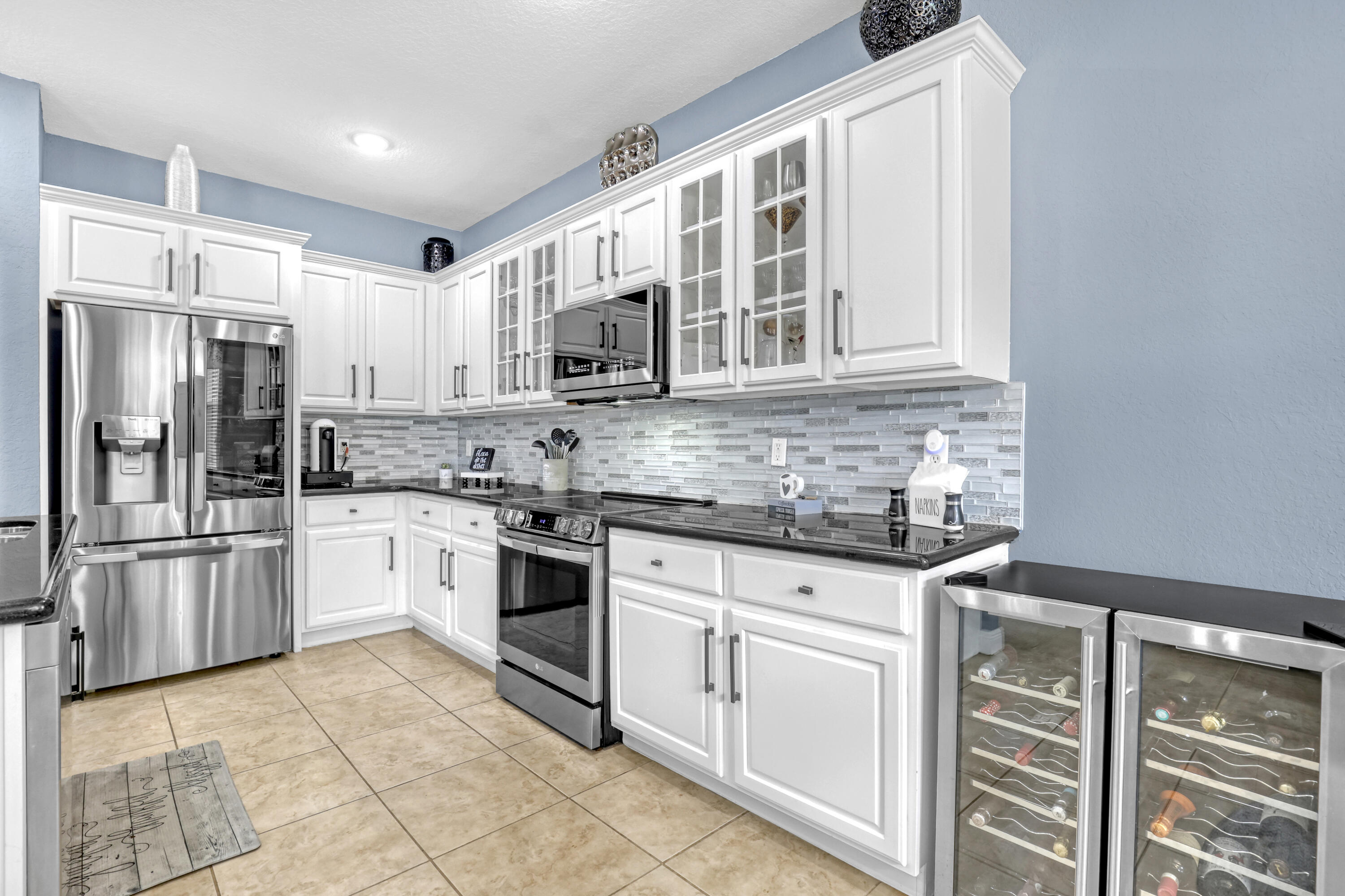 Kitchen featuring white shaker-style cabinetry with glass-front accents, polished granite countertops, stainless steel appliances, a linear-patterned tile backsplash