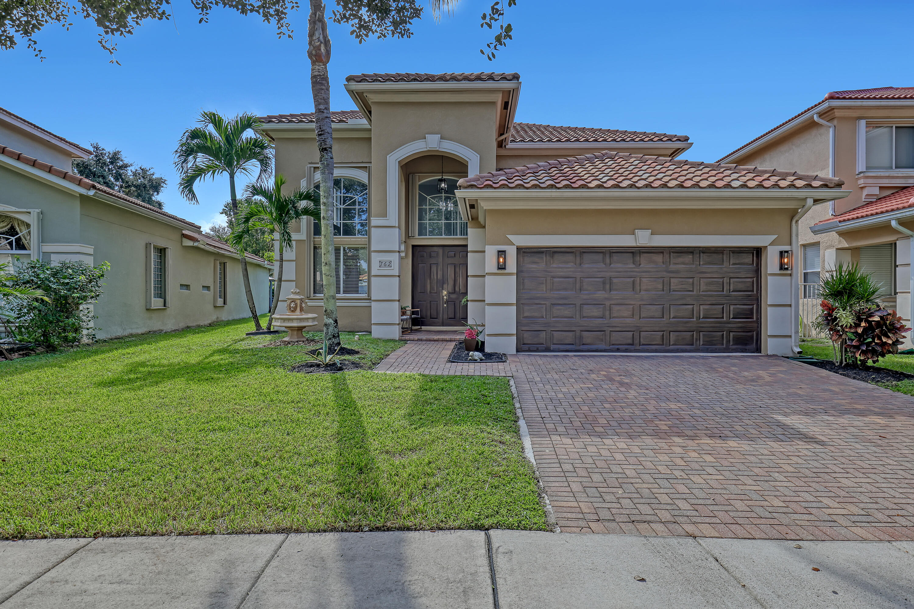 Stucco exterior with decorative quoins, arched entryway, tile roof, brick-paver driveway, and double-door entry