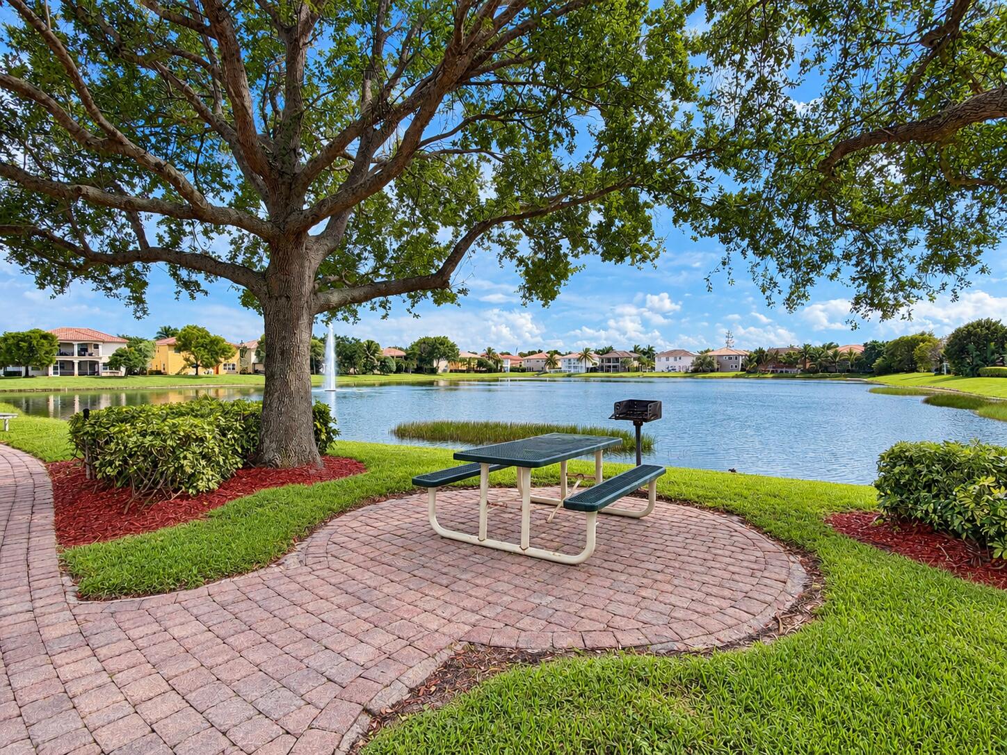 Waterfront common area featuring a paved brick walkway, mature shade tree, manicured lawn