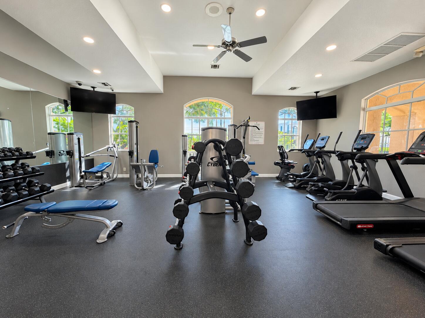 Fitness center featuring high ceilings, recessed lighting, rubberized flooring, ceiling fan, and arched windows
