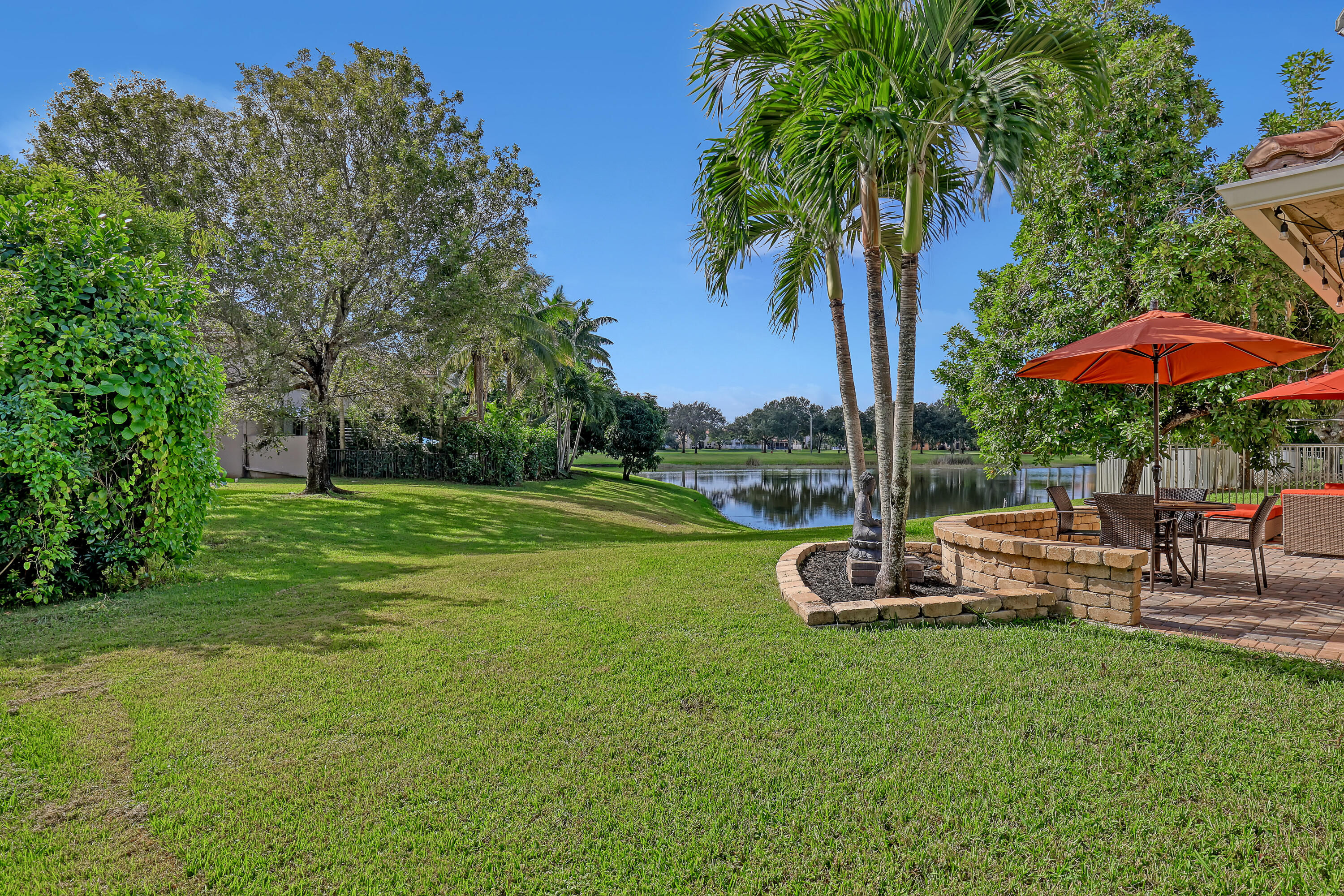 Expansive lawn, water frontage, mature palms, and brick-paver patio with a stone-finish retaining wall