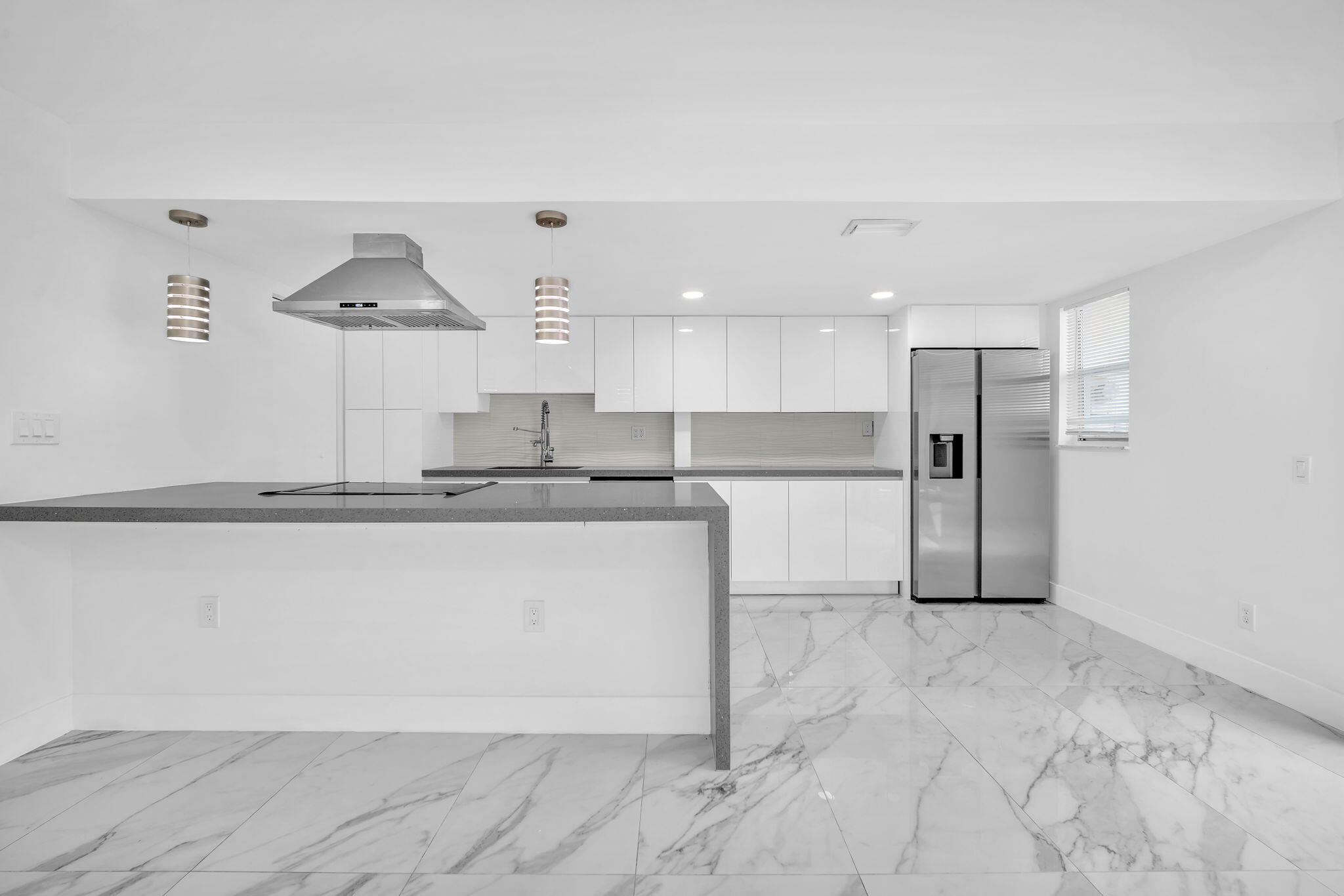 Kitchen featuring white flat-panel cabinetry, quartz countertops, a stainless steel range hood, stainless steel refrigerator, and stone-finish flooring
