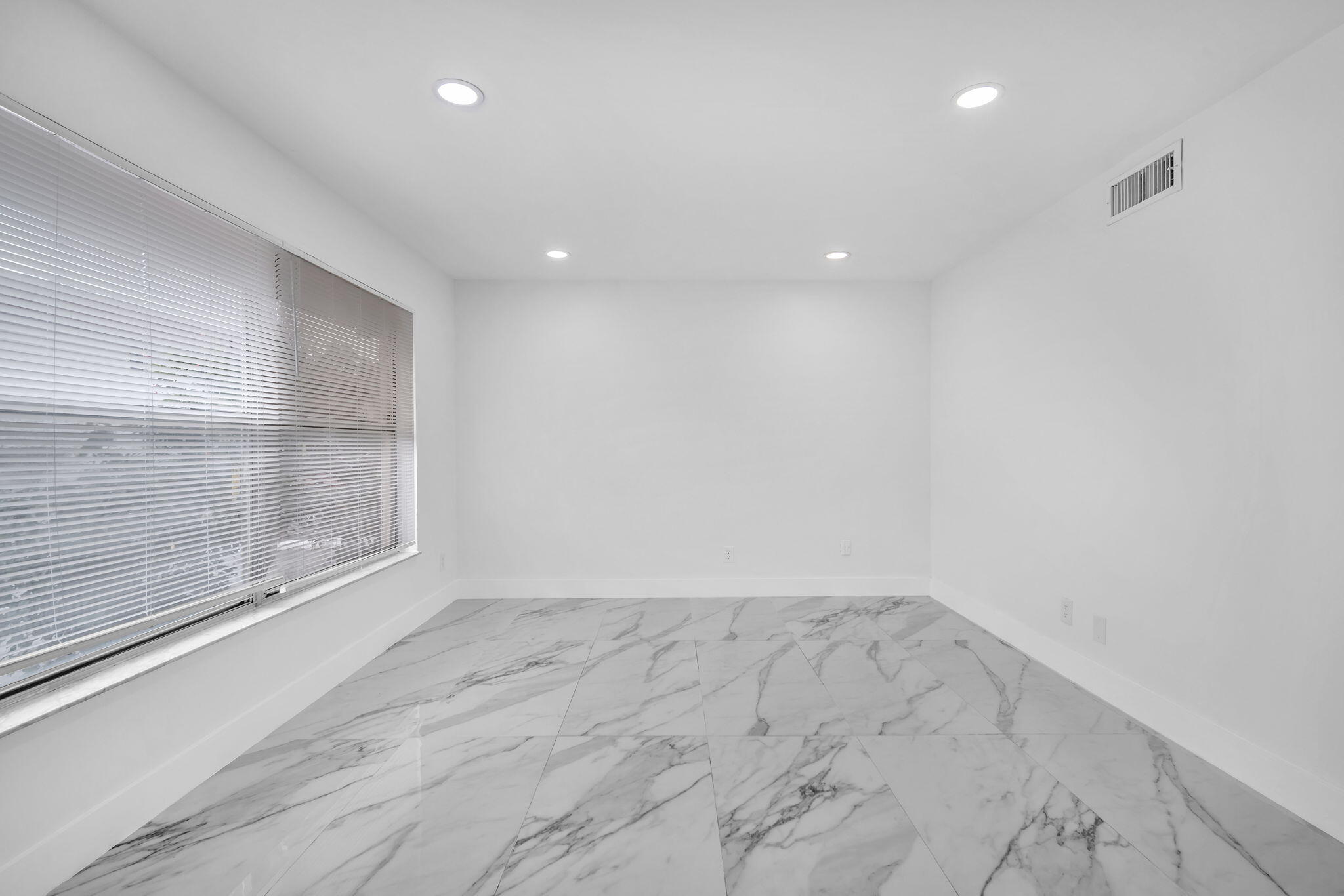 Interior space featuring large-format veined tile flooring, recessed ceiling lighting, and windows equipped with fitted horizontal blinds
