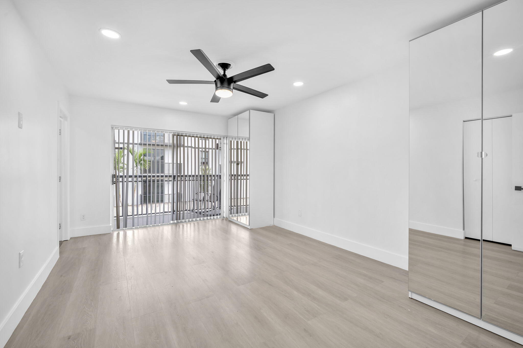Light-filled room featuring wood-finish flooring, recessed lighting, a modern ceiling fan, and floor-to-ceiling mirrored closet doors