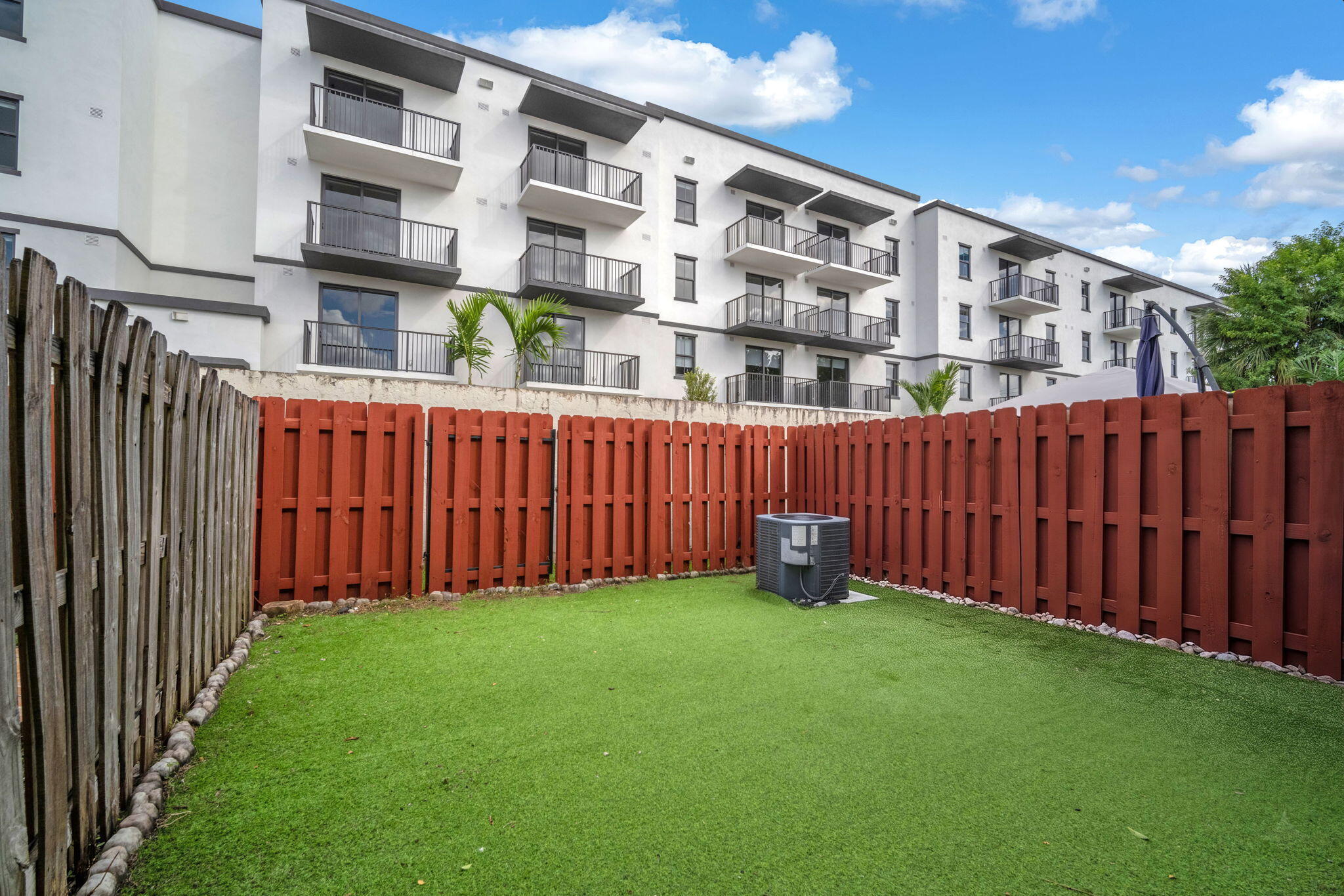 Private fenced yard featuring synthetic turf and a multi-story exterior facade with tiered balconies