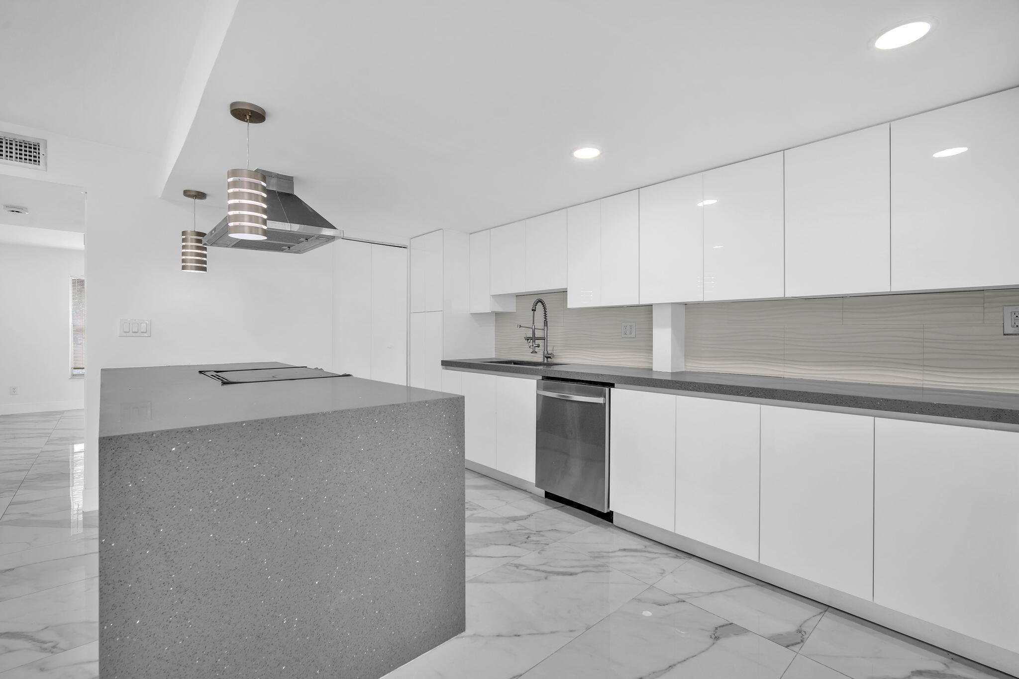 Modern kitchen featuring high-gloss white cabinetry, a large central island with a solid-surface countertop, recessed ceiling lighting, stainless steel appliances, and large-format tile flooring